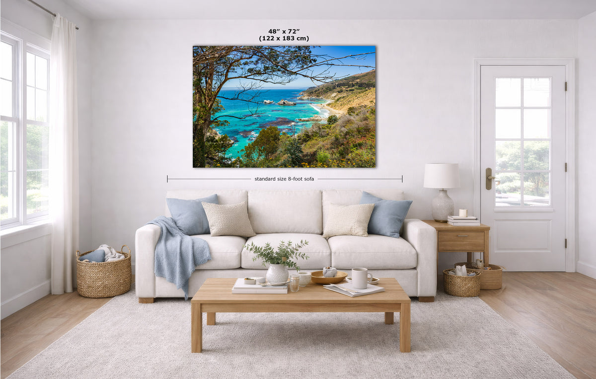 A landscape canvas print of a coastal bay with turquoise water, green hills, and trees, displayed on a white wall in a modern living room mockup with dimension lines and text indicating its size.