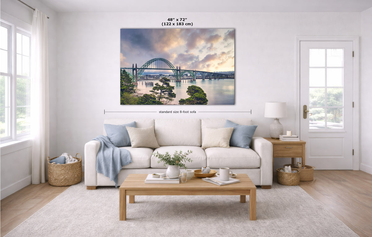 A large rectangular wall art print showing a bridge over water at sunset, displayed above a white sofa in a bright modern living room. Measurement lines and text indicate the print size as 48 x 72 inches.