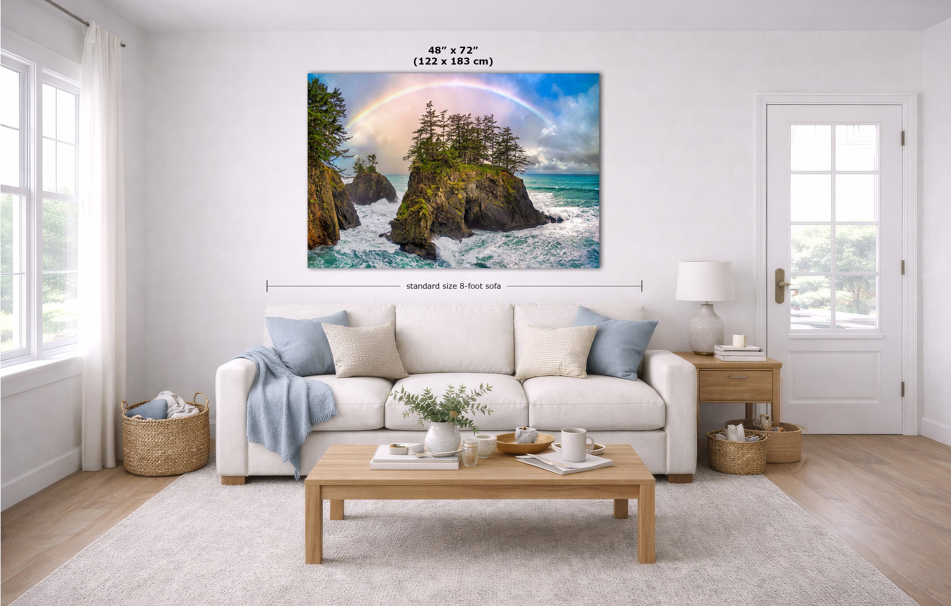 A large rectangular wall art print showing a coastal rocky shoreline with ocean waves, green trees, and a rainbow, displayed above a white sofa in a bright living room. Measurement text and arrows indicate the print size as 48 x 72 inches.