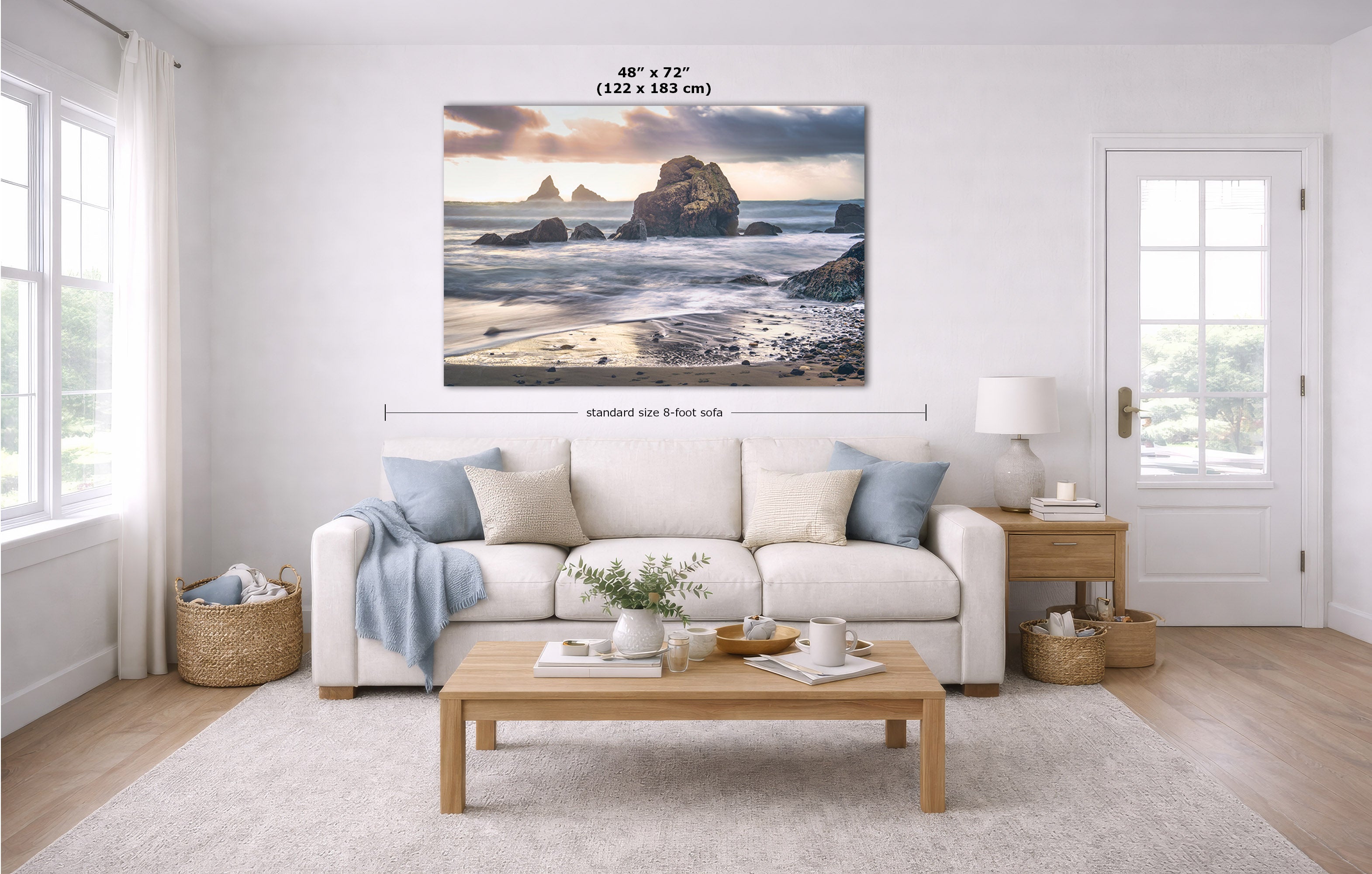 A large rectangular wall art print showing a coastal rock formation at sunset, displayed above a white sofa in a bright modern living room. Measurement lines and text indicate the print size as 48 x 72 inches.