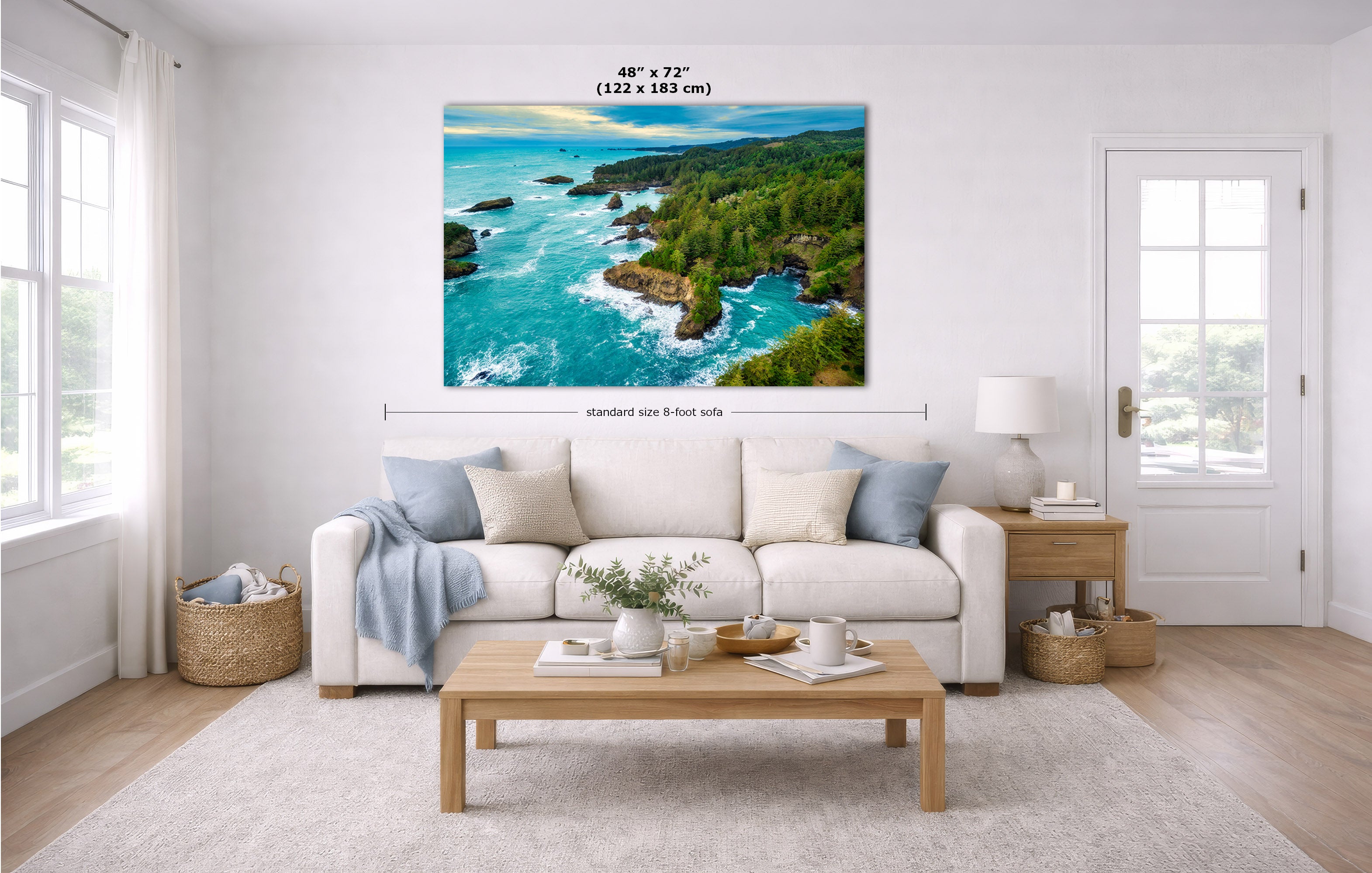 A square wall art print showing a coastal landscape with turquoise water, rocky shoreline, and green trees, displayed above a white sofa in a bright living room. Measurement labels and text indicating 48 x 72 inches are overlaid on the artwork.