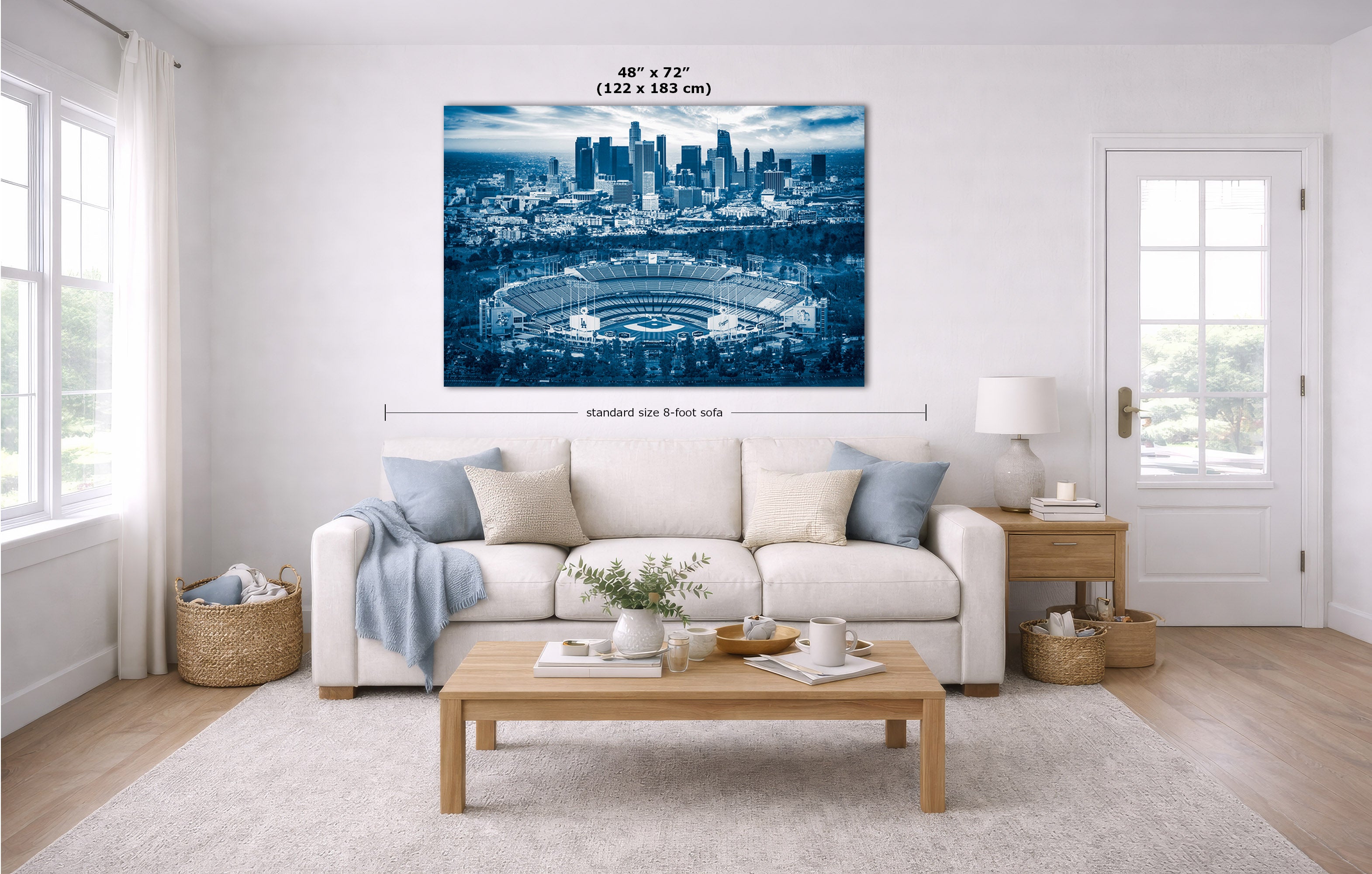 A Dodger Stadium skyline wall art print showing a blue-toned stadium and city skyline, displayed above a white sofa in a bright living room. Measurement lines and text indicate the print size as 48 x 72 inches.