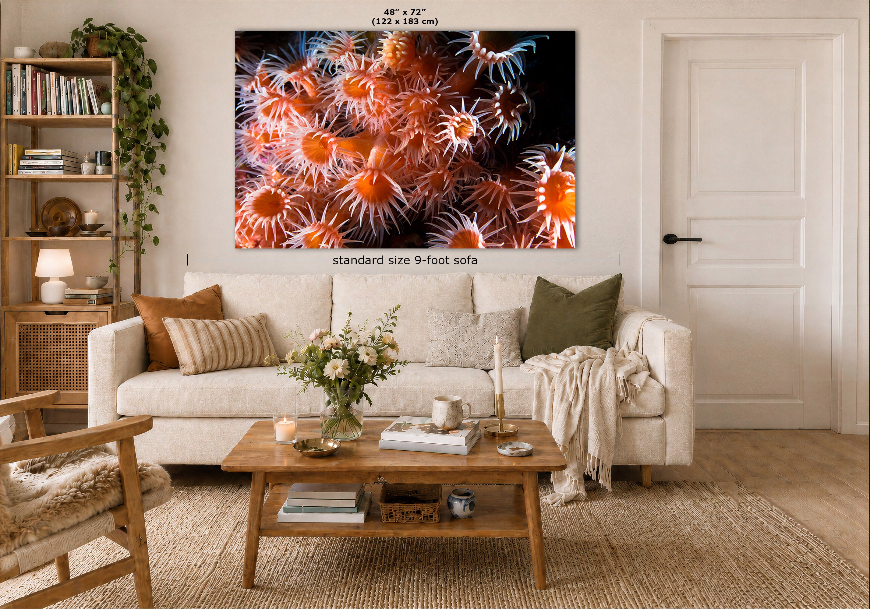 A large wall art print showing a close-up of orange and white sea anemones on a black background, displayed above a white sofa in a styled living room. Measurement text indicates the print is 48 x 72 inches, and a dimension line notes standard size 9-foot sofa.