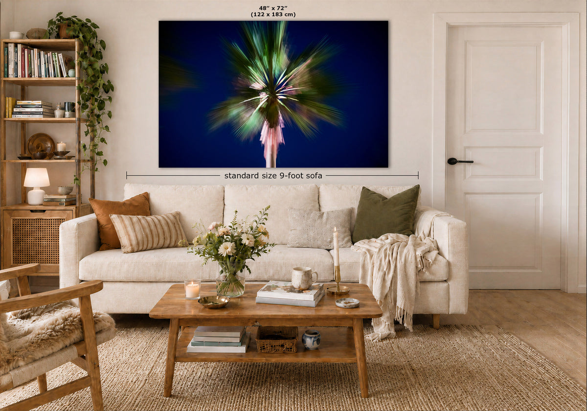 A large wall art print displayed above a white sofa in a styled living room. The artwork shows a colorful abstract burst of light on a dark blue background, with measurement labels indicating 48 x 72 inches and standard size 9-foot sofa context.