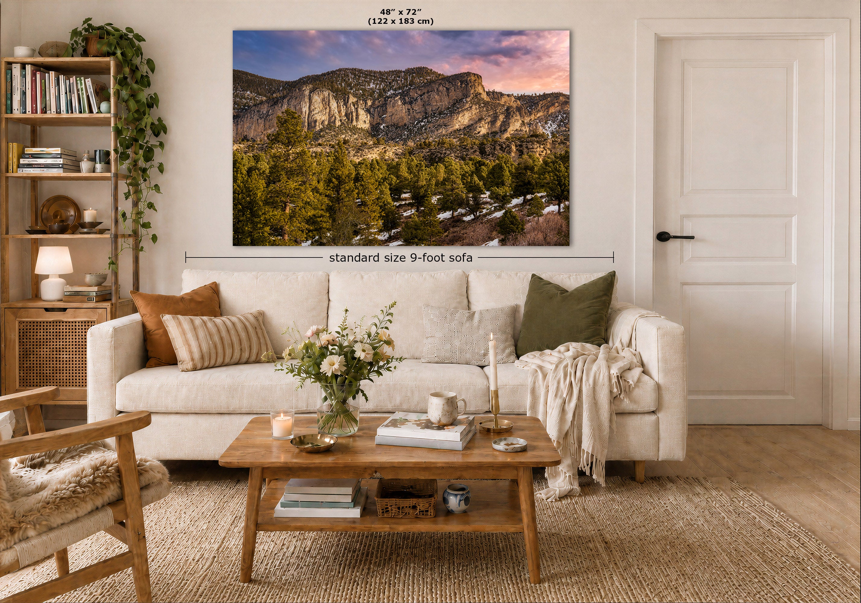 A large wall art print showing a mountain landscape with trees and a sunset sky, displayed above a white sofa in a styled living room. Measurement text indicates the print is 48 x 72 inches, and the room scene includes a sofa, coffee table, bookshelf, and door.