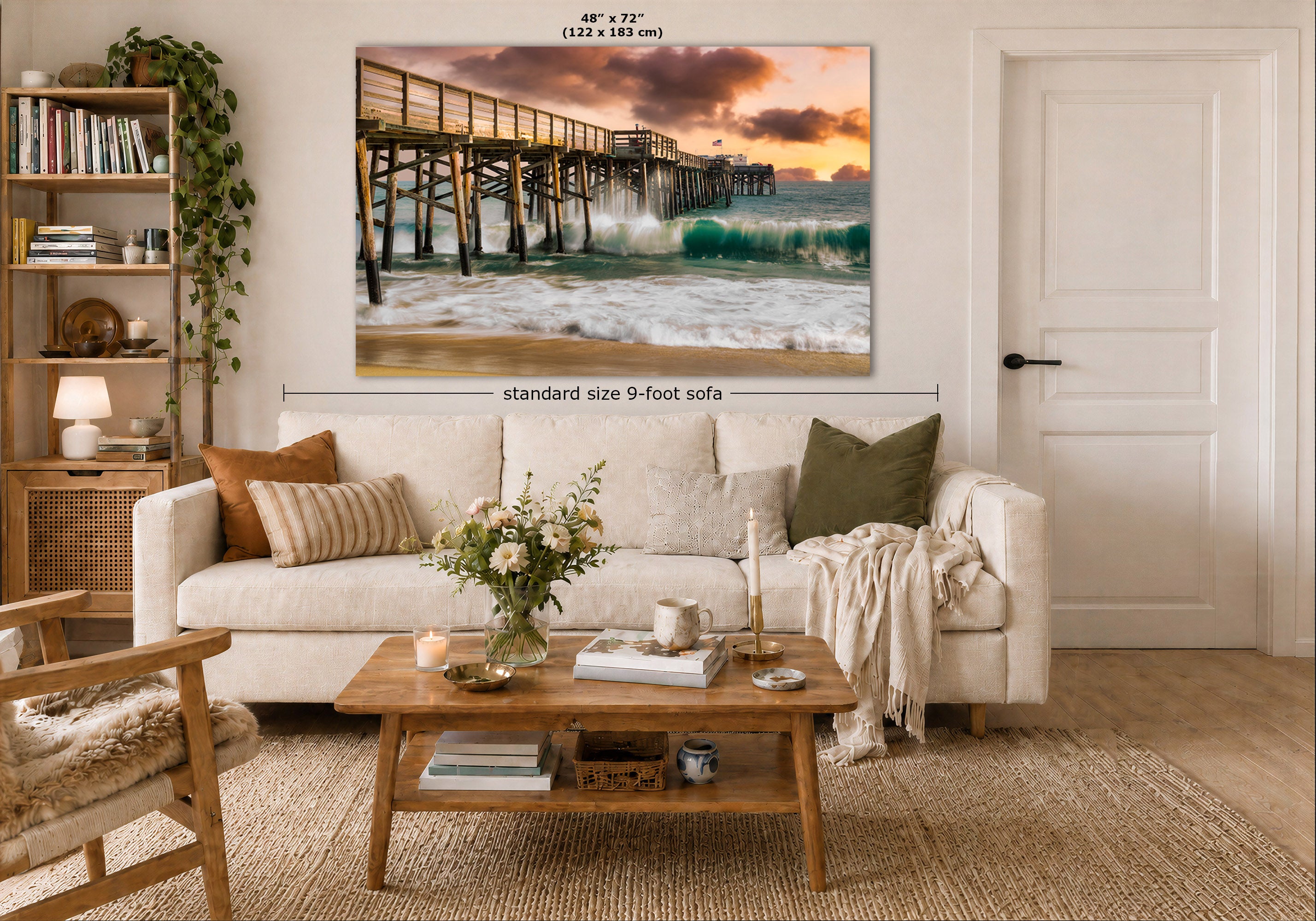 A large wall art print of a pier and ocean waves hangs on a wall above a white sofa in a styled living room. The image includes dimension labels indicating the canvas is 48 x 72 inches (122 x 183 cm) and the sofa is standard size 9-foot.
