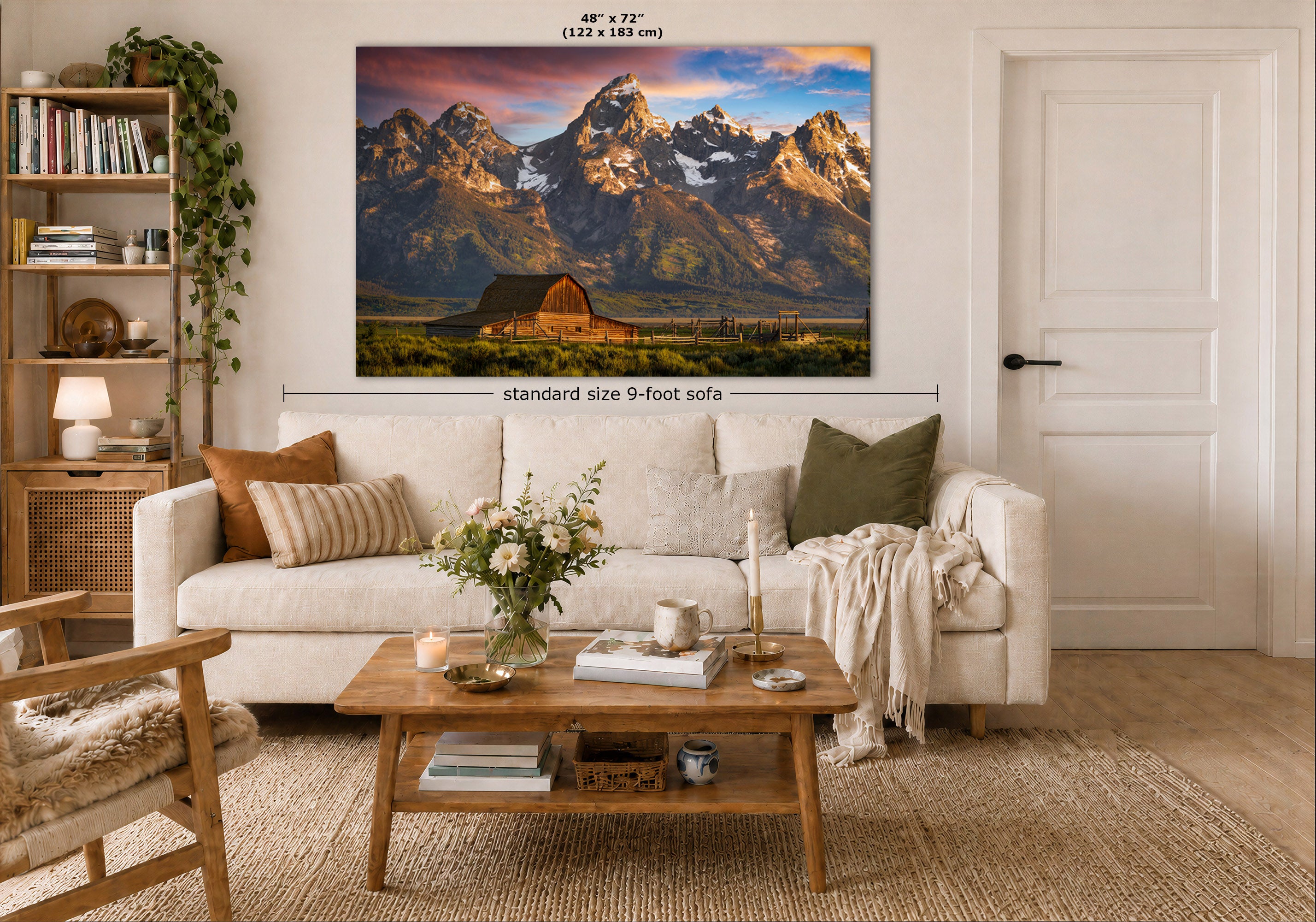 A large wall art print showing snow-capped mountain peaks at sunrise hangs above a white sofa in a styled living room. White text above the print indicates dimensions, and a smaller text label reads 'standard size 9-foot sofa'.
