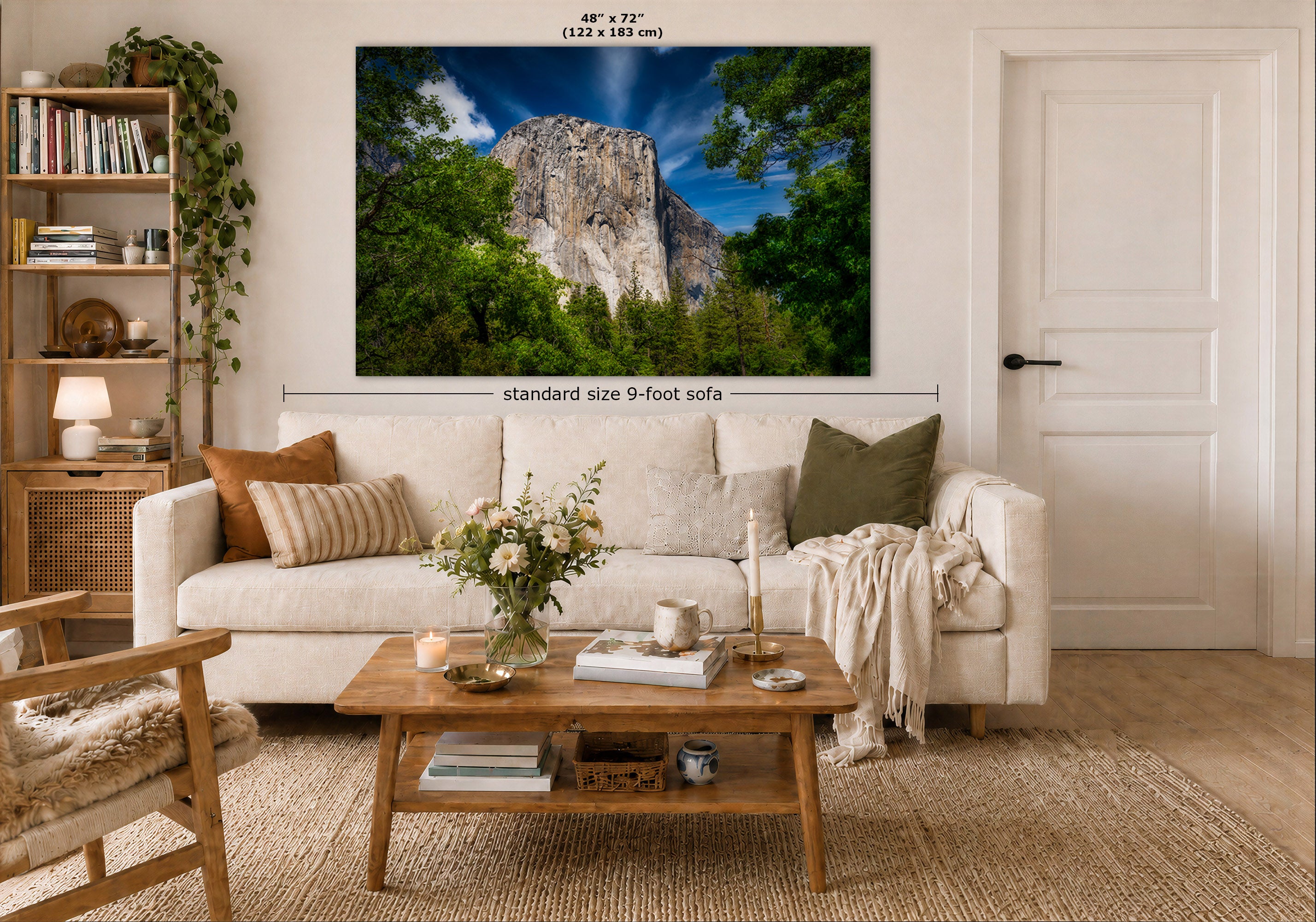 A wall art print of a mountain landscape in Yosemite Valley is displayed above a white sofa in a modern, well-lit living room. The print features a tall rocky cliff surrounded by lush green trees under a blue sky.