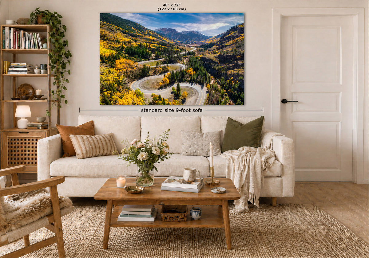 A large wall art print showing a winding road through a colorful mountain valley, displayed above a white sofa in a styled living room. Text on the image indicates the print size as 48 x 72 inches.