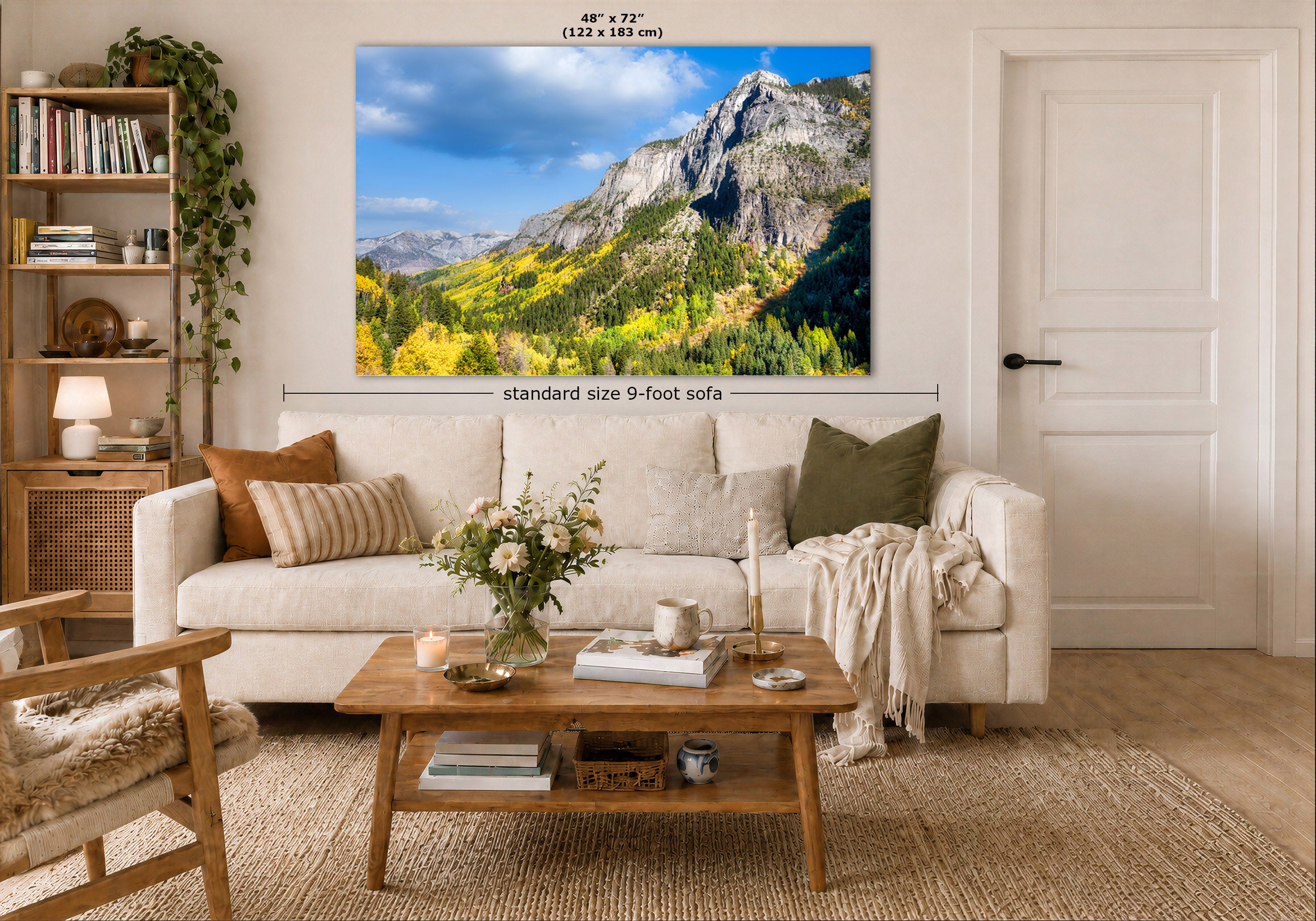 A large framed wall art print showing a mountain landscape with blue sky and autumn foliage, displayed above a cream sofa in a styled living room. Measurement text and arrows indicate the print size as 48 x 72 inches (122 x 183 cm).
