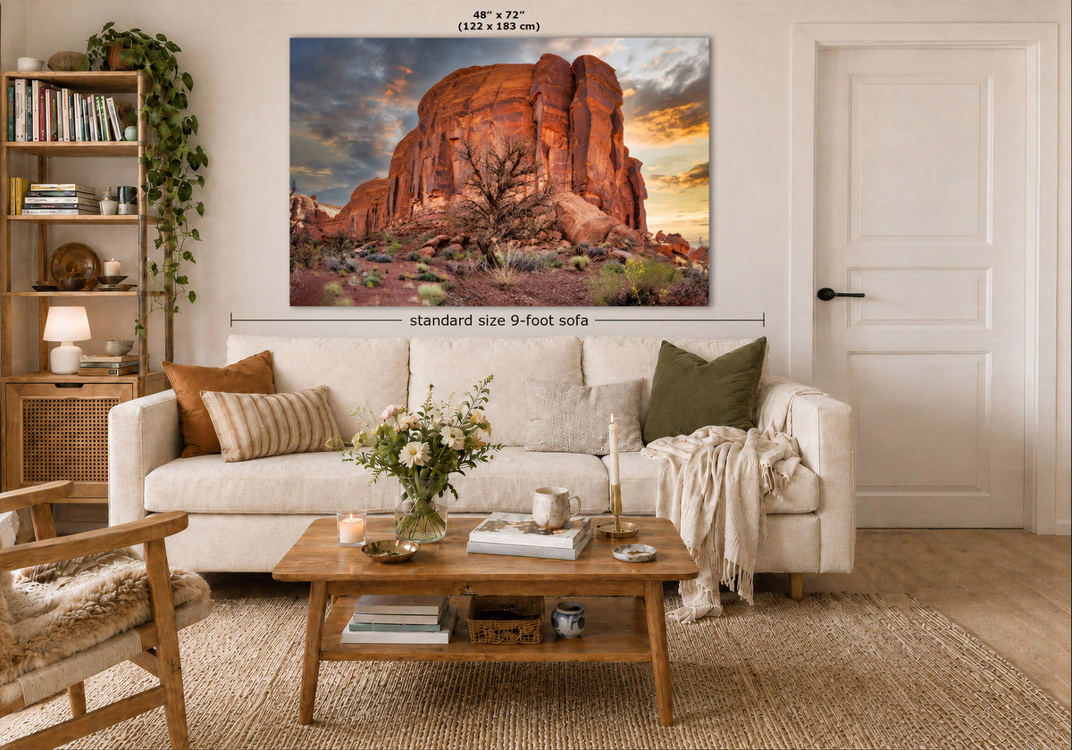 A large wall art print of a desert rock landscape is displayed above a white sofa in a styled living room. The print shows a dramatic orange and brown canyon scene at sunset.