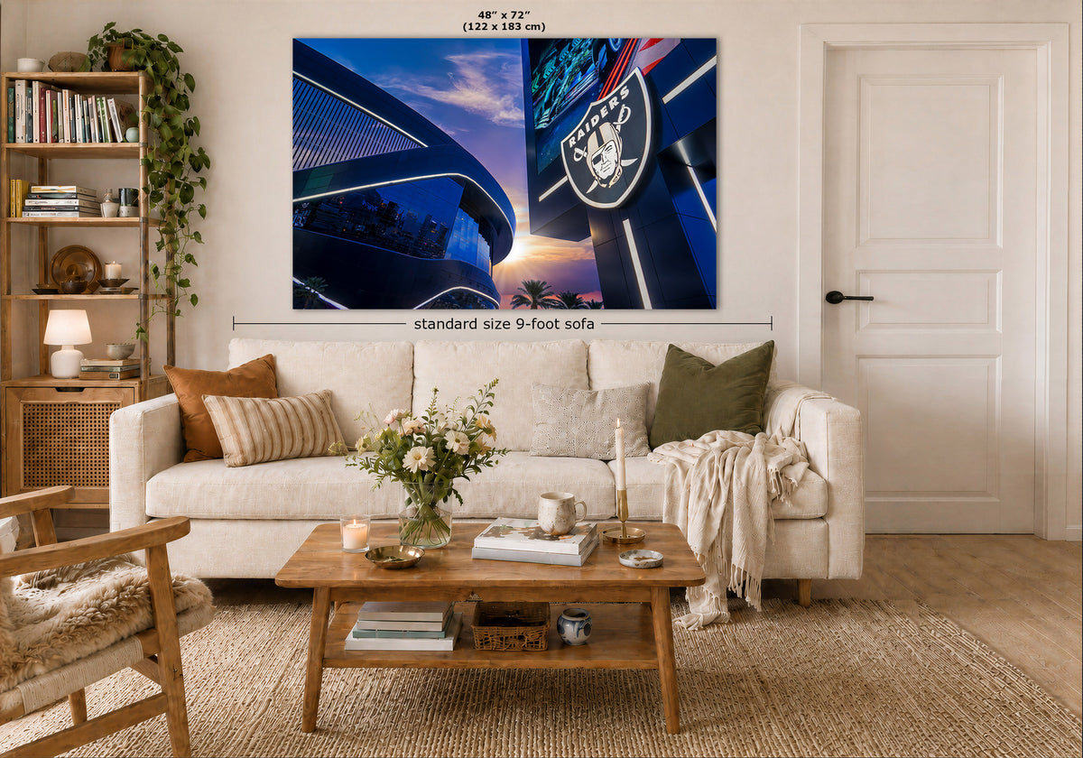 A large wall art print showing a blue-toned stadium scene with the Raiders logo is displayed above a white sofa in a styled living room. Measurement labels indicate 48 x 72 inches and standard size 9-foot sofa context.