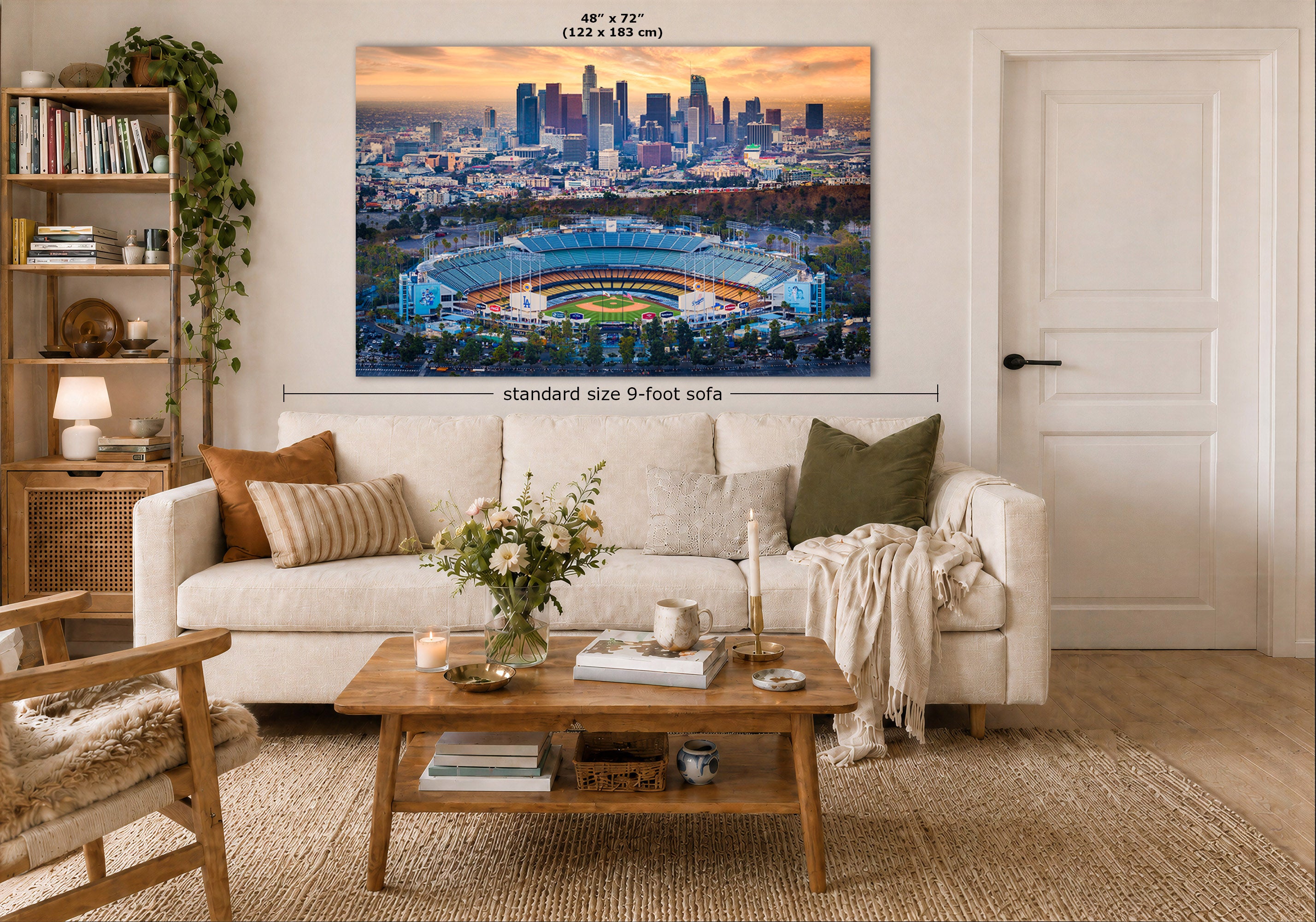 A large framed wall art print showing the Los Angeles skyline and Dodgers Stadium at sunrise, displayed above a white sofa in a styled living room. Measurement text and arrows indicate the print size as 48 x 72 inches (122 x 183 cm), with a note about a standard size 9-foot sofa.