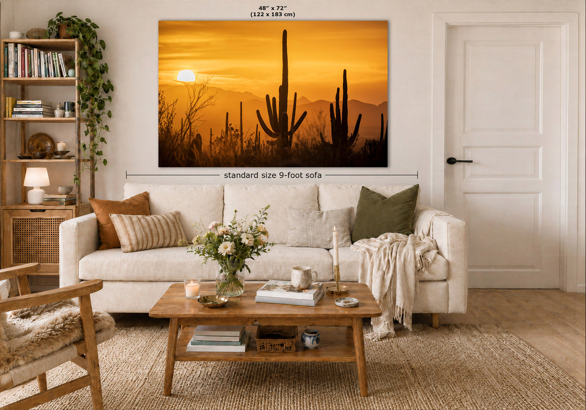 A large wall art print showing a desert sunset with cactus silhouettes, displayed above a white sofa in a styled living room. The print includes dimension labels indicating 48 x 72 inches (122 x 183 cm) and a note reading standard size 9-foot sofa.