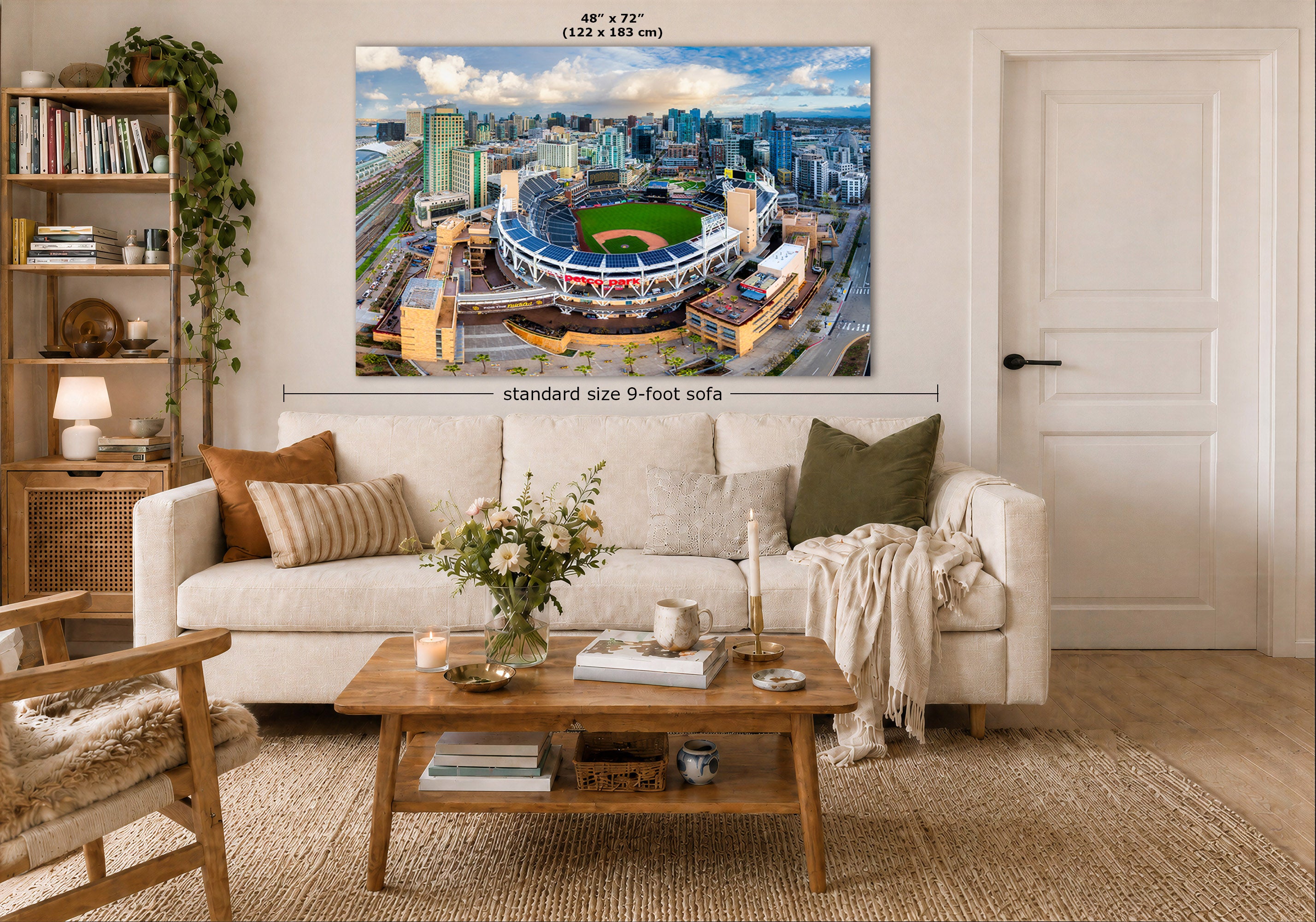 A San Diego Padres skyline art print of a stadium and cityscape hangs above a white sofa in a styled living room. The print shows a blue sky, urban skyline, and green field.