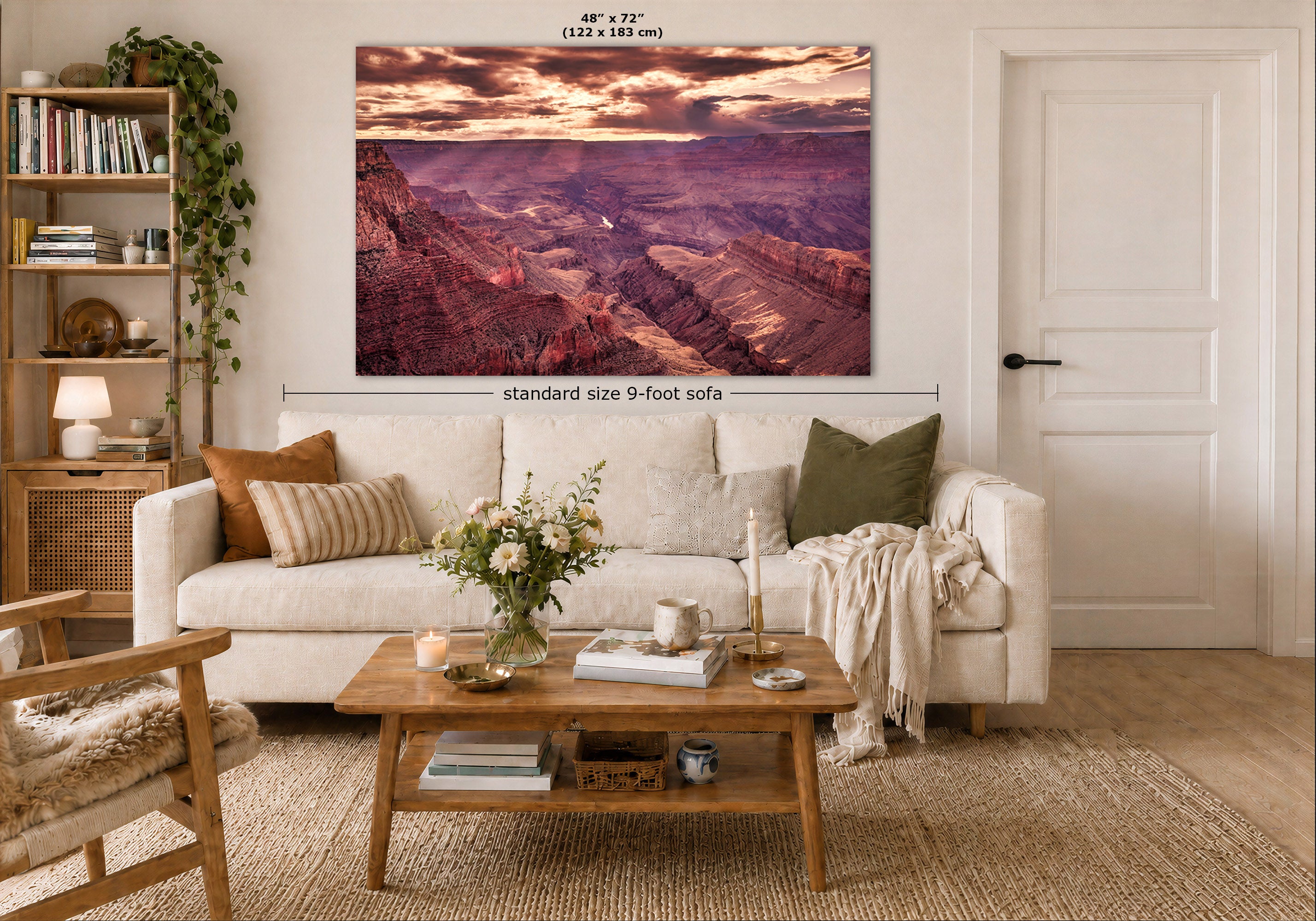 A large rectangular wall art print showing a canyon landscape in warm sunset tones, displayed above a white sofa in a styled living room. White text labels indicate the print size as 48 x 72 inches (122 x 183 cm) and include a dimension callout for a standard 9-foot sofa.