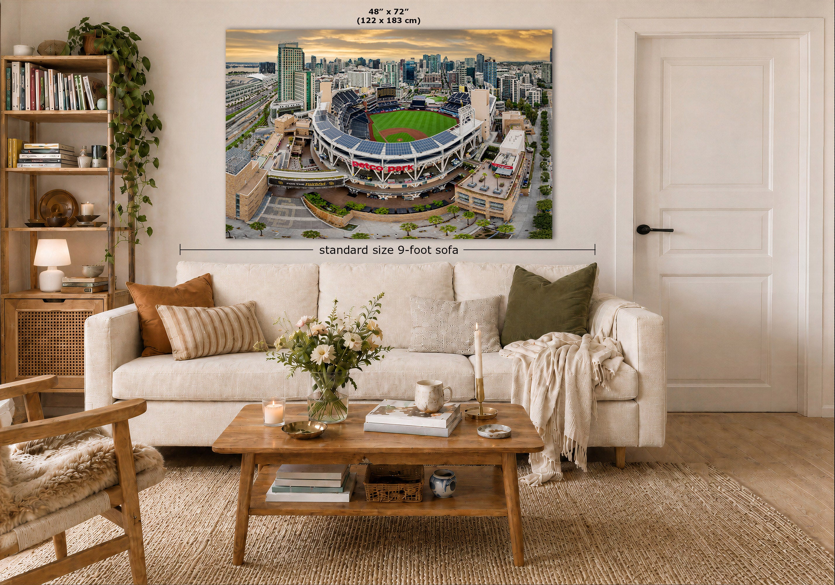 A large wall art print of an aerial stadium scene displayed above a white sofa in a styled living room. The print includes dimension labels reading 48 x 72 inches at the top and 'standard size 9-foot sofa' with a measurement line below.