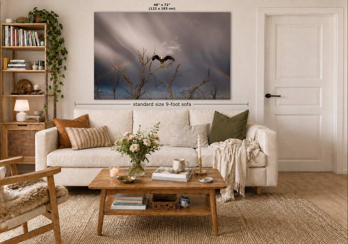 A wall art print showing a dramatic stormy sky with bare tree branches and a faint rainbow, displayed above a white sofa in a styled living room. Measurement text indicates the print is 48 x 72 inches, and a dimension line notes the standard size 9-foot sofa below.
