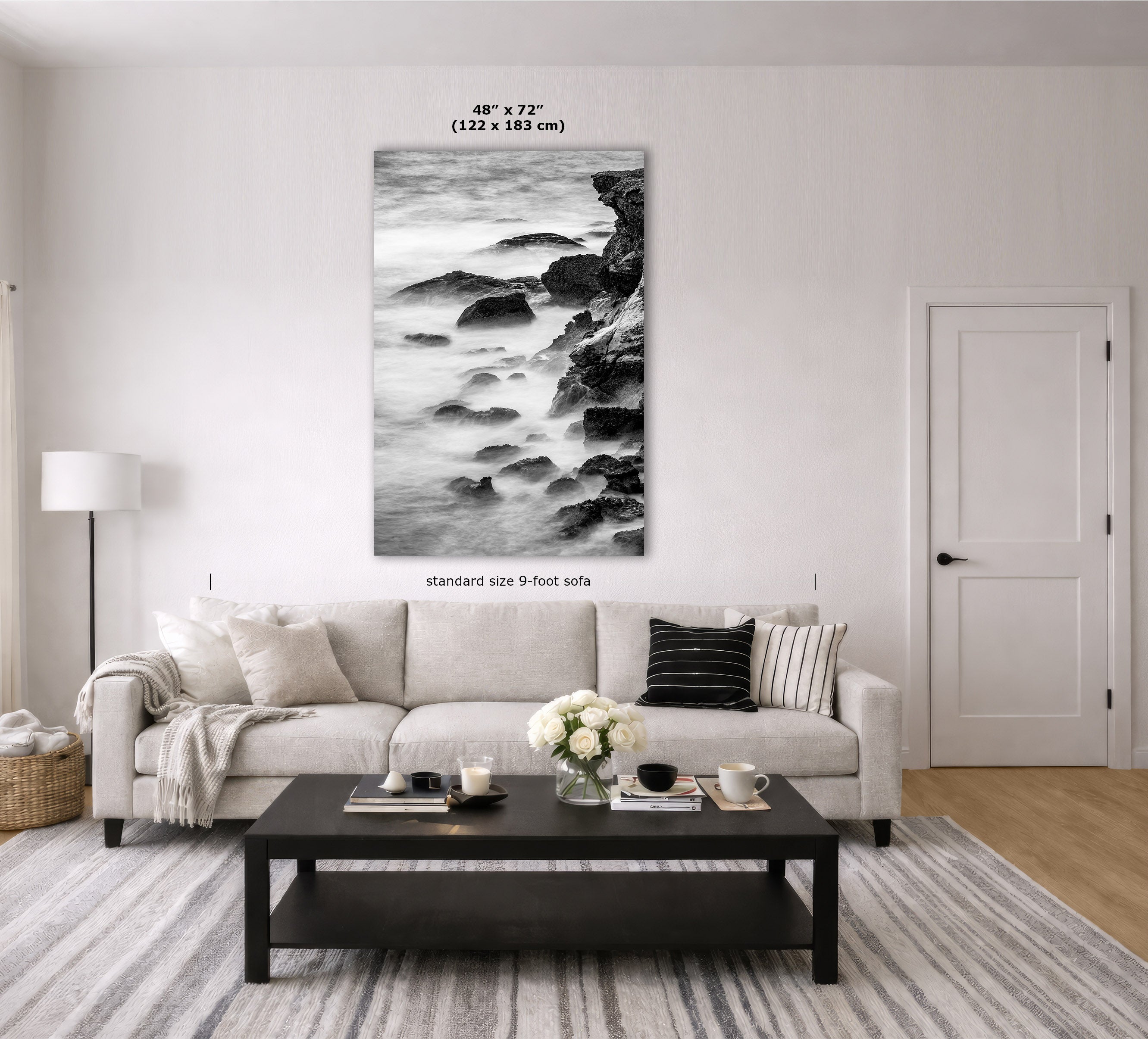 A black and white coastal rock wall art print is displayed above a light beige sofa in a modern living room. The image includes dimension labels indicating the print is 48 x 72 inches (122 x 183 m) and the sofa is standard size 9 feet wide.