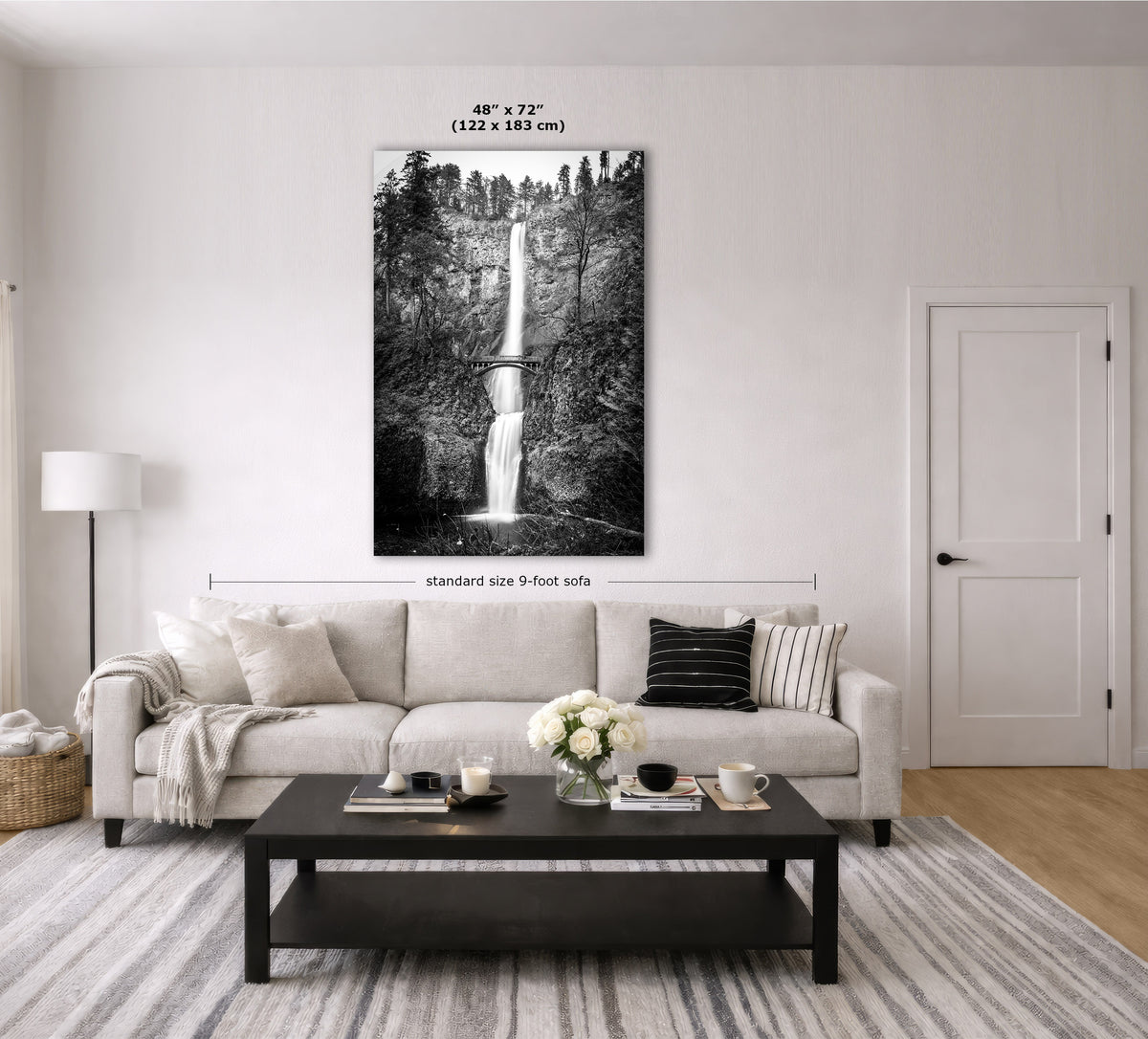 A black and white waterfall wall art print displayed above a light beige sofa in a modern living room. The image includes dimension labels indicating the print is 48 x 72 inches (122 x 183 m) and the sofa is standard size 9 feet tall.