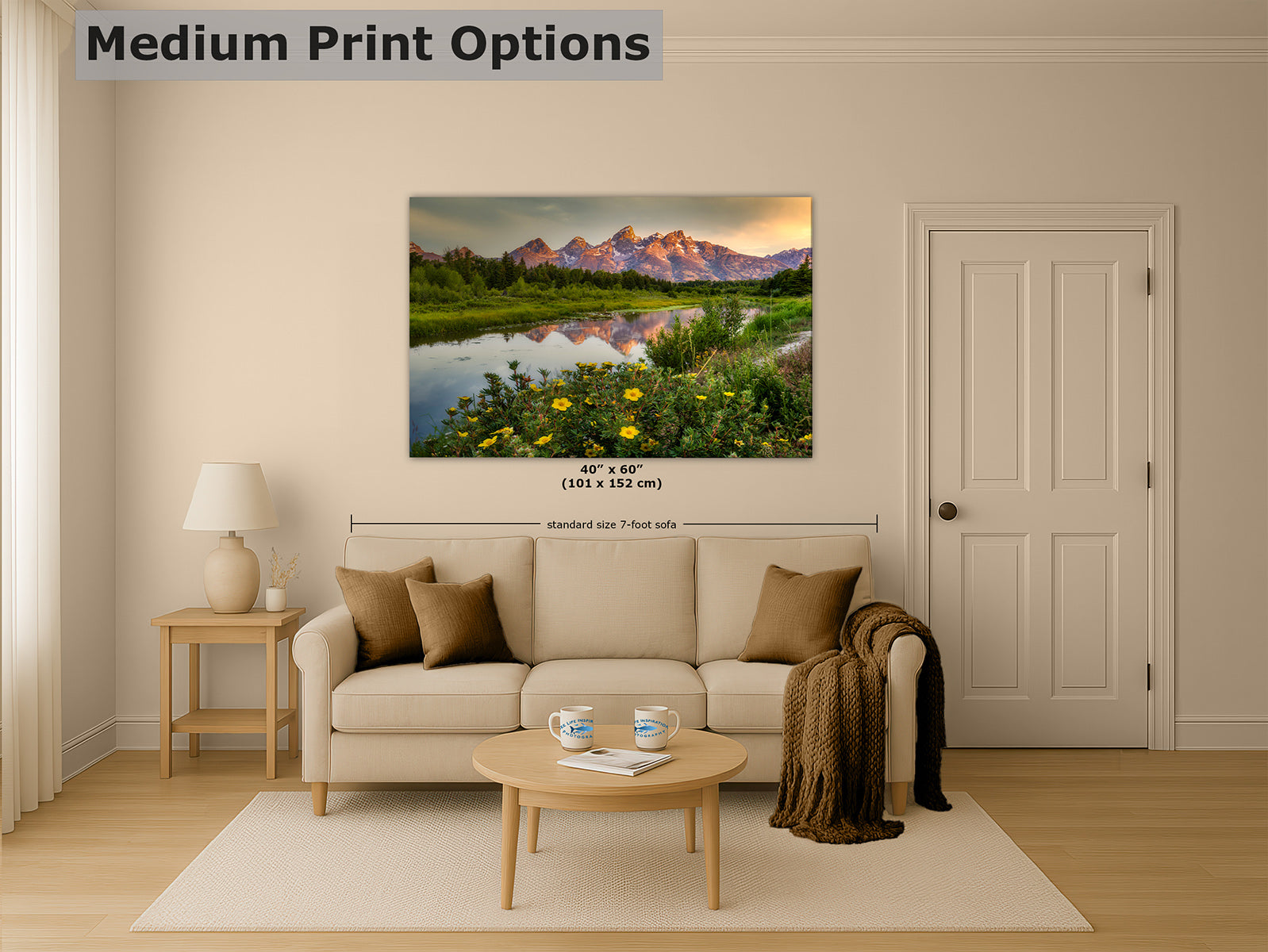 A framed landscape wall art print of the Grand Teton Mountains showing mountains over a river with yellow flowers, displayed above a beige sofa in a styled living room. The image includes the text 'Medium Print Options' and size markings for the print.