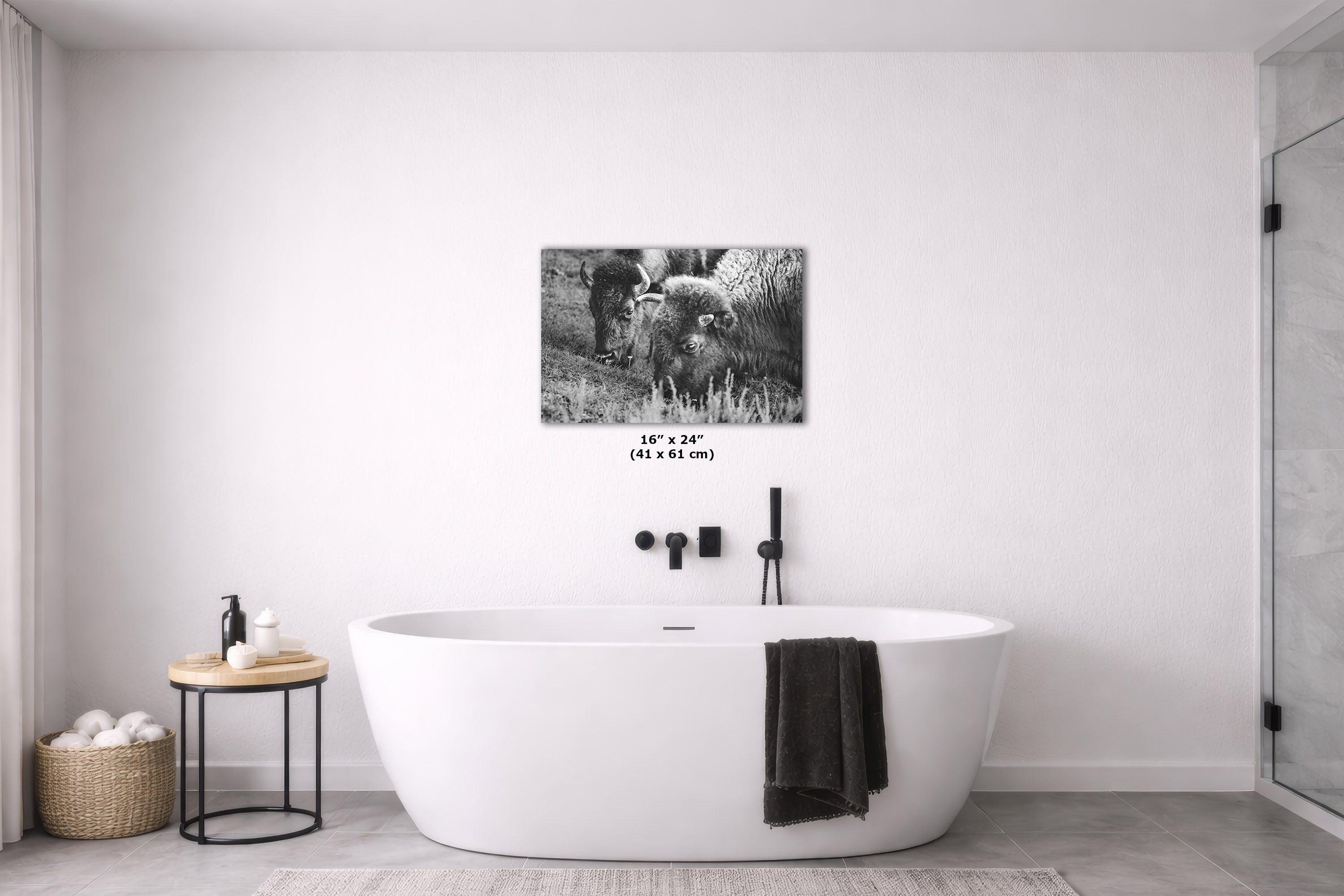 A black and white canvas wall art print depicting bison in a field, styled in a modern bathroom setting above a freestanding bathtub.