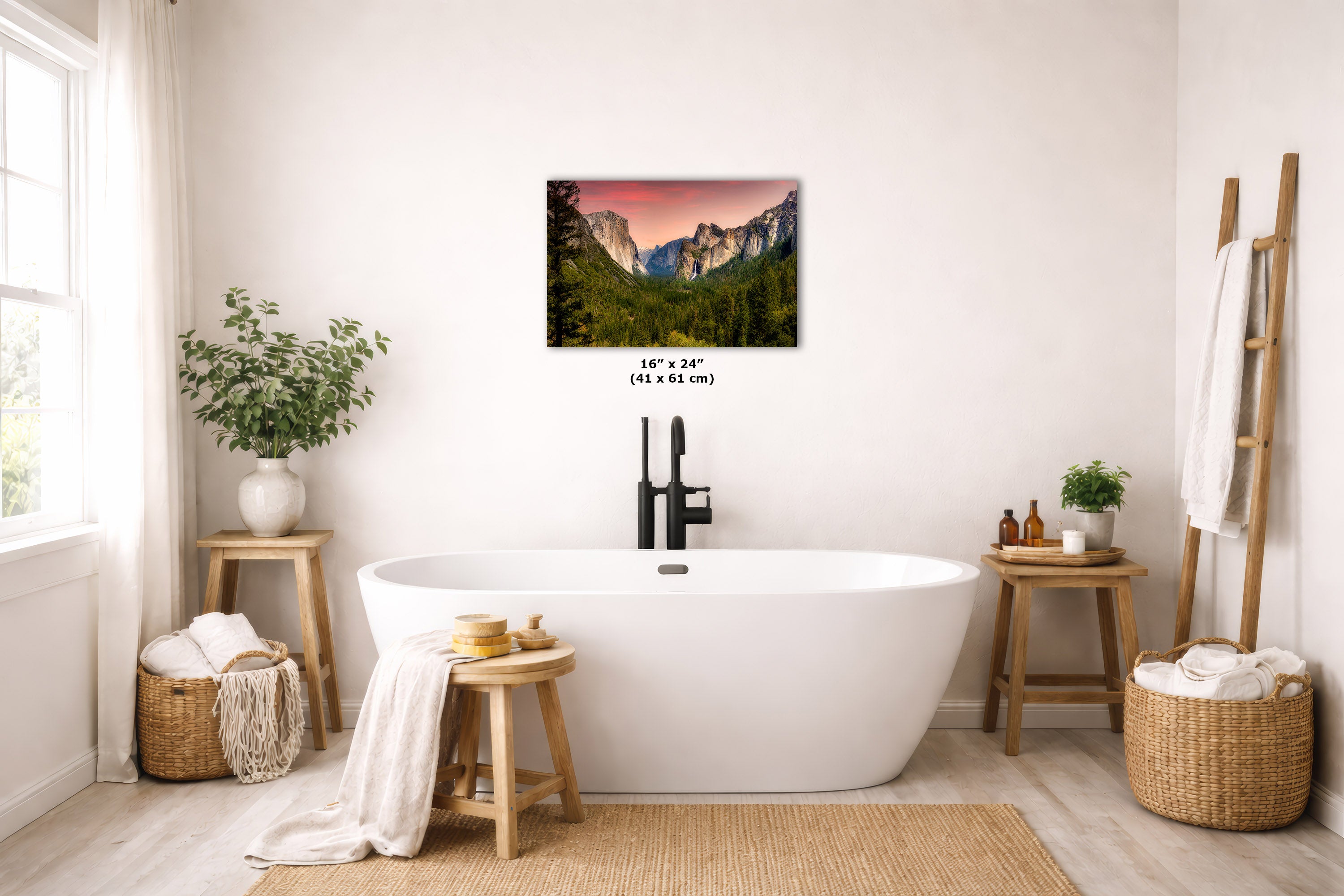 A wall art print depicting a waterfall in a rocky mountain landscape, displayed above a white freestanding bathtub in a bright, modern bathroom with wooden stools, plants, and woven baskets.