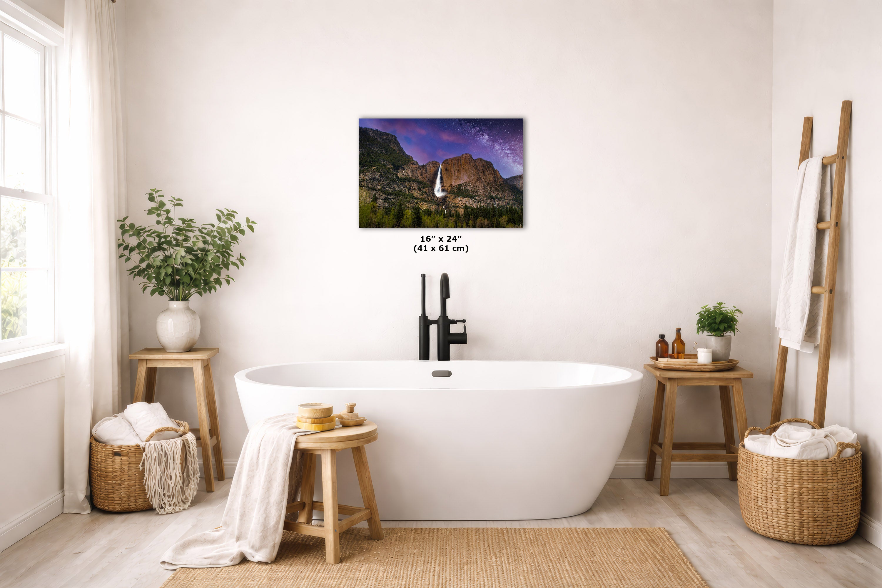 A wall art print showing a waterfall in a mountain landscape hangs above a freestanding white bathtub in a bright, neutral bathroom. The print includes size text reading 16 x 24 (41 x 61 cm).