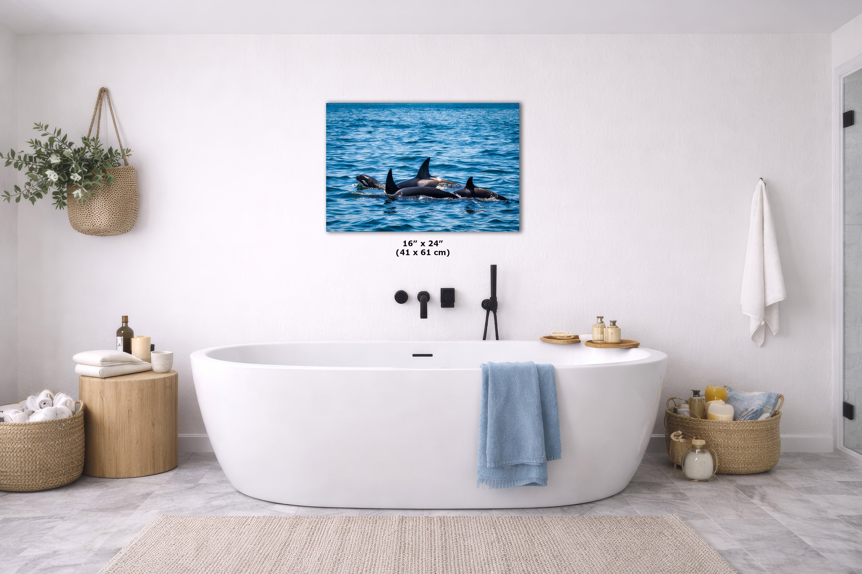 A blue-toned wall art print hangs above a freestanding white bathtub in a bright, modern bathroom with coastal decor and a blue towel draped over the tub.