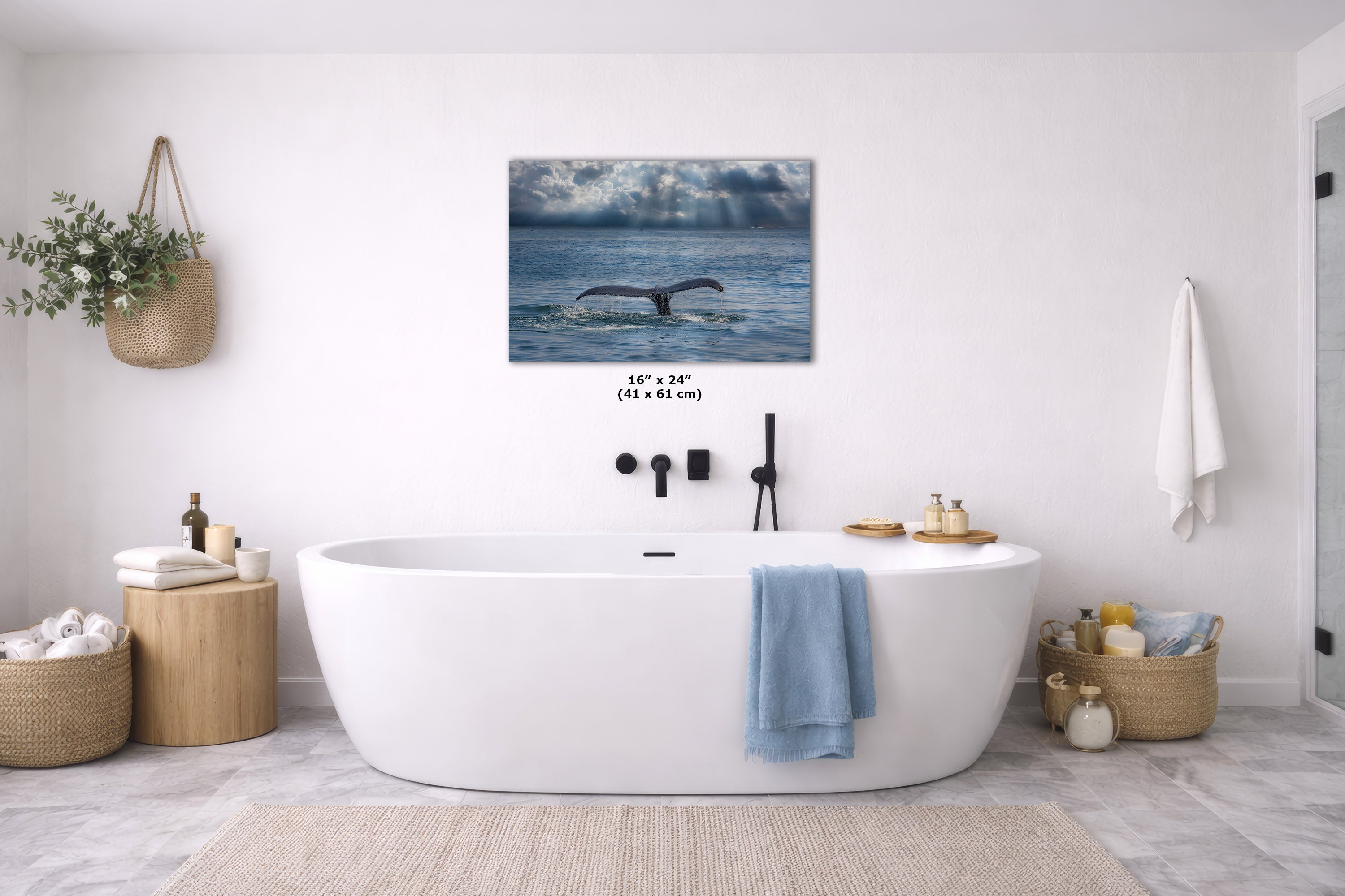 A wall art print showing a whale tail in blue ocean water, displayed above a white freestanding bathtub in a bright, modern bathroom. The print includes size text reading 16 x 24" (41 x 61 in).