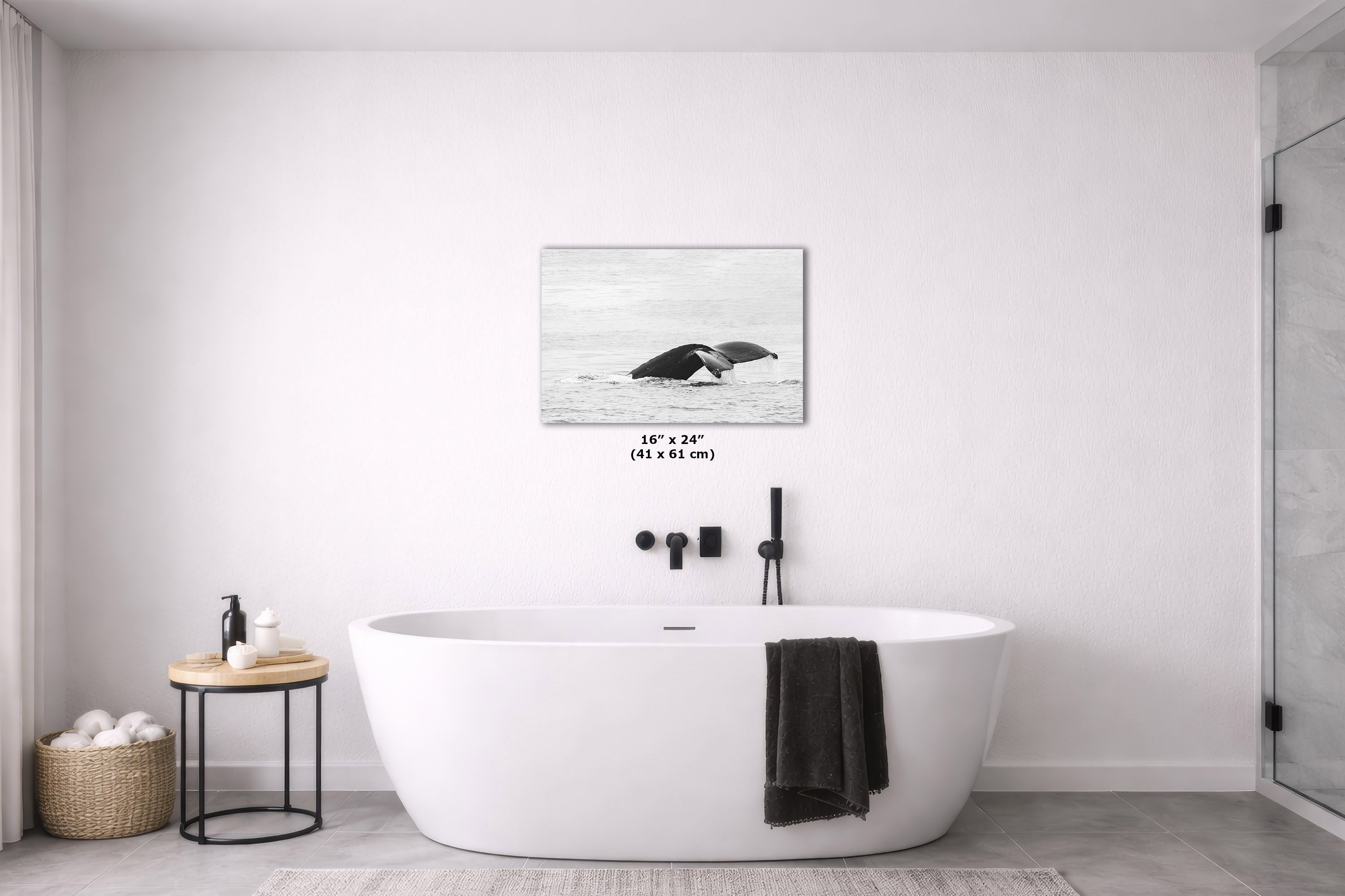 A whale print hanging on a white bathroom wall above a freestanding white bathtub. The print shows a black-and-white whale in water, with size text below it.