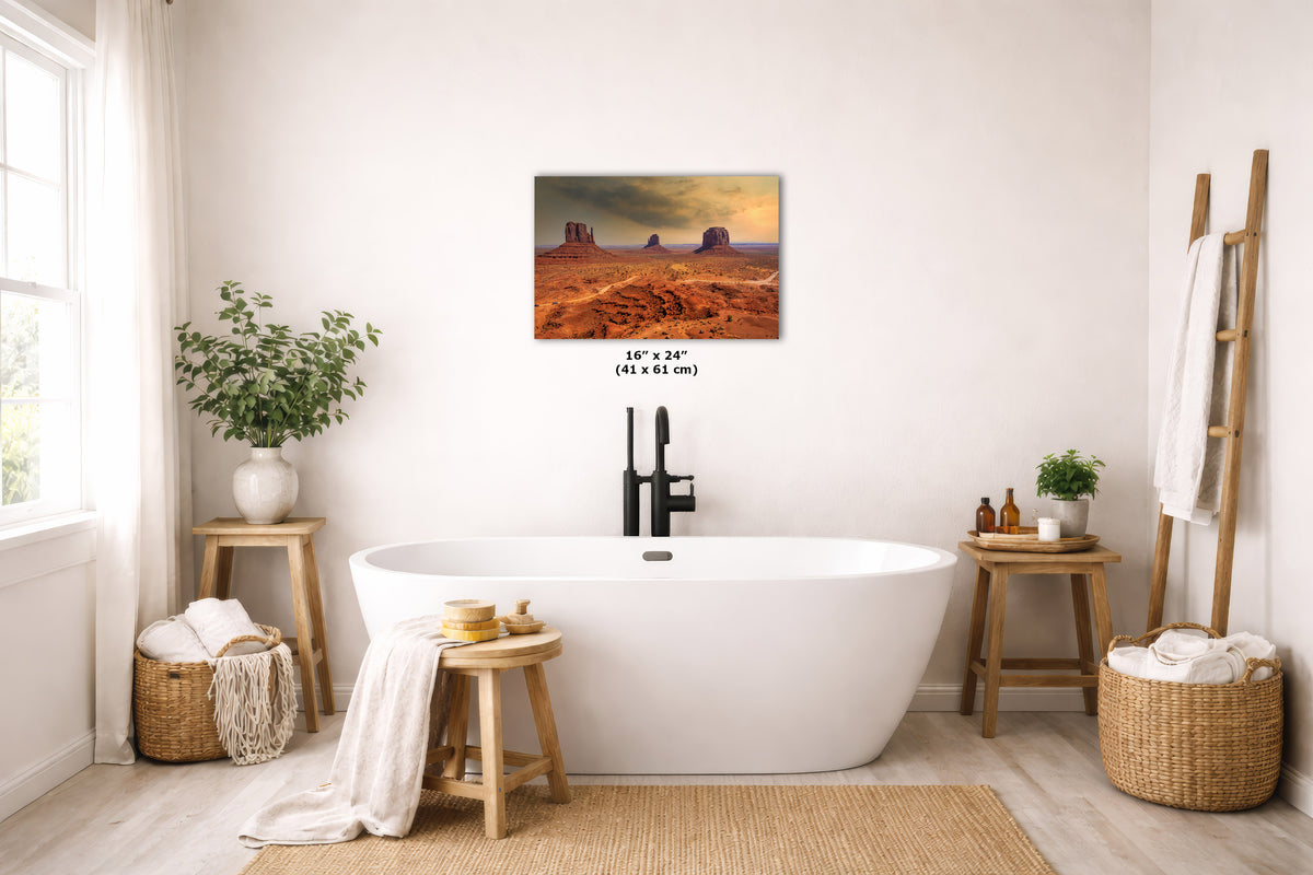 A desert landscape wall art print hangs above a freestanding white bathtub in a bright, neutral-toned bathroom. The artwork depicts orange and brown desert rock formations under a warm sky.