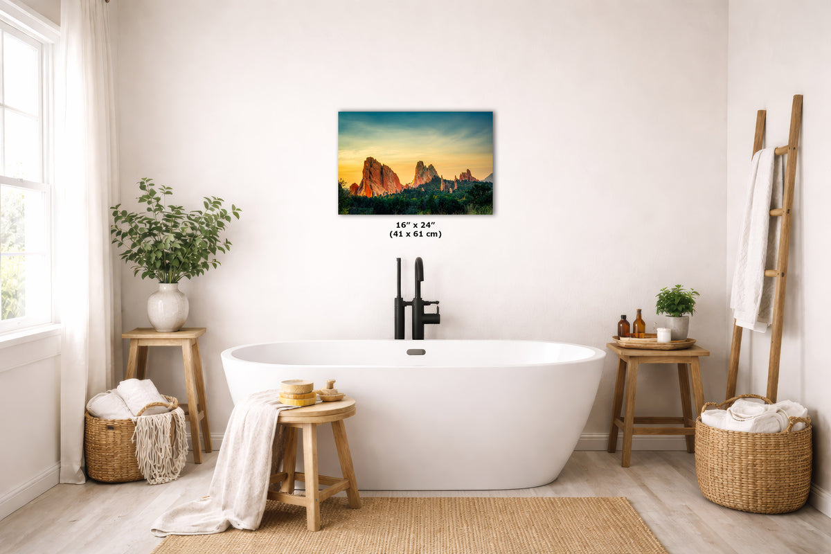 A wall art print showing a colorful mountain sunset hangs above a white freestanding bathtub in a bright, neutral bathroom. The print includes a small size label reading 16 x 24 in (41 x 61 cm).