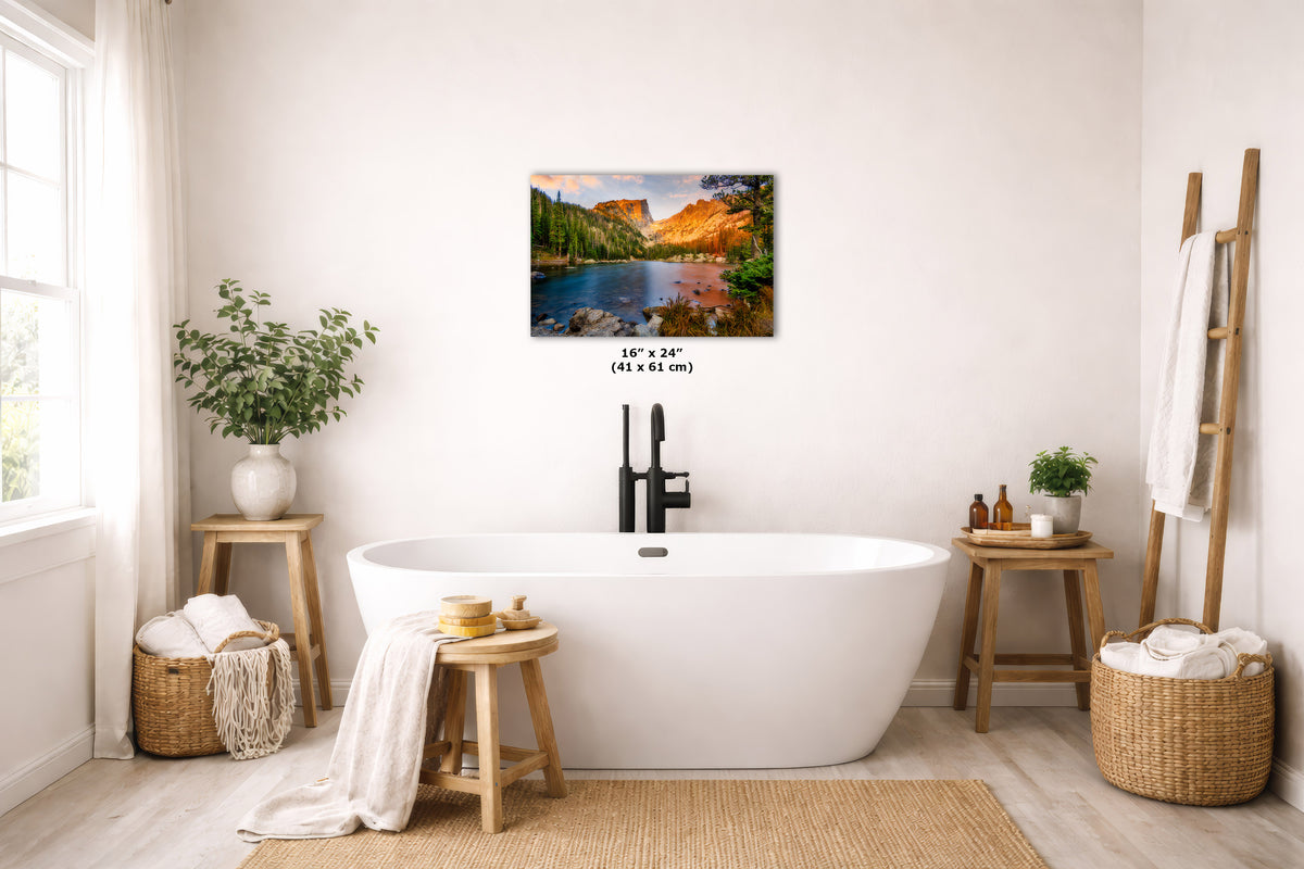 A wall art print showing a colorful mountain lake landscape hangs above a white freestanding bathtub in a bright, neutral-toned bathroom. The print includes a small size label reading 16 x 24 (41 x 61 cm).