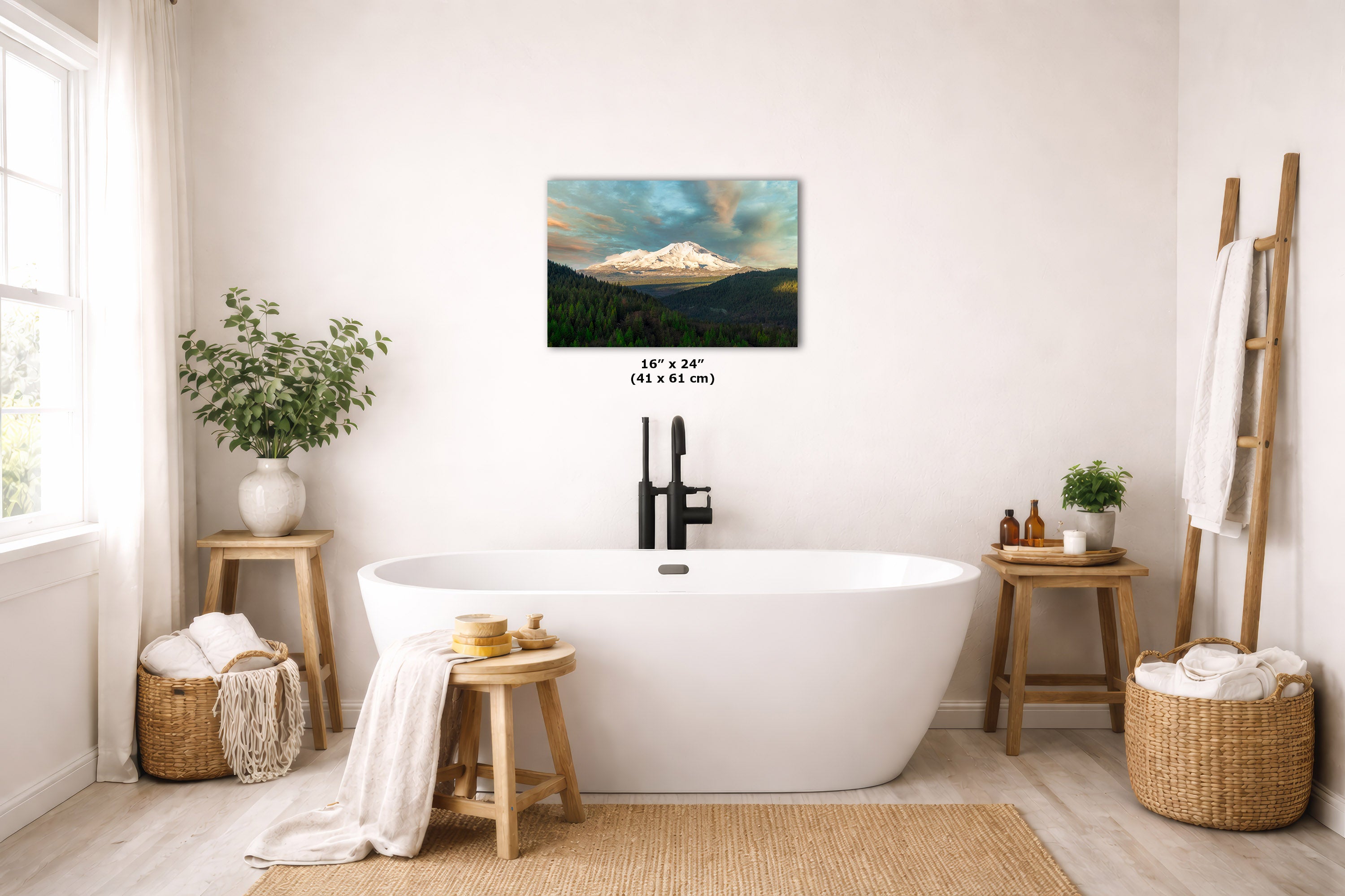 A wall art print depicting a mountain landscape with a glowing sunrise is displayed above a freestanding white bathtub in a bright, modern bathroom. The print is shown with its dimensions printed below it.