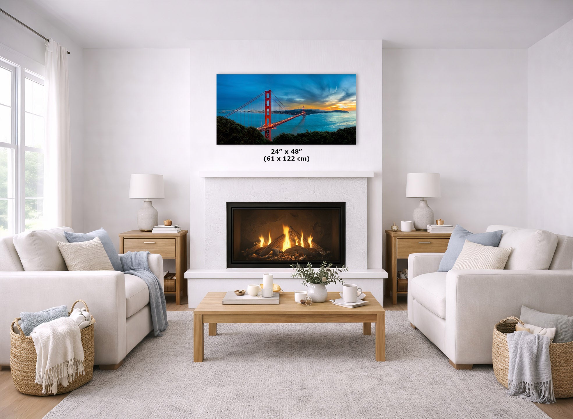 A framed wall art print of the Golden Gate Bridge hangs above a fireplace in a bright, modern living room with two white sofas, a wooden coffee table, and neutral decor. The print includes a size measurement overlay reading 24" x 48" (61 x 122 cm).