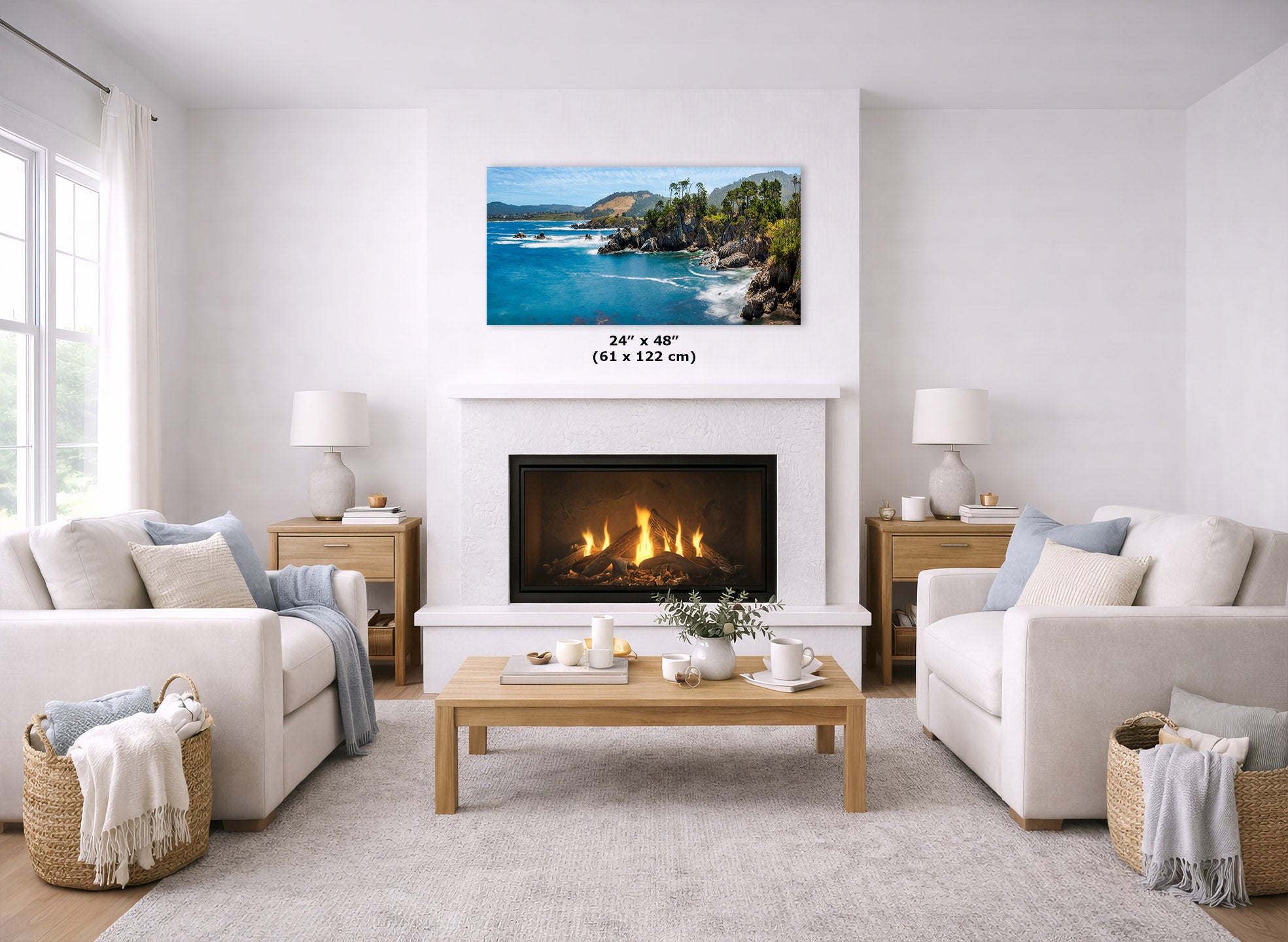 A framed landscape wall art print showing a tropical beach and rocky coastline hangs above a fireplace in a bright, modern living room. The print is labeled with dimensions 24" x 48" (61 x 122 cm).