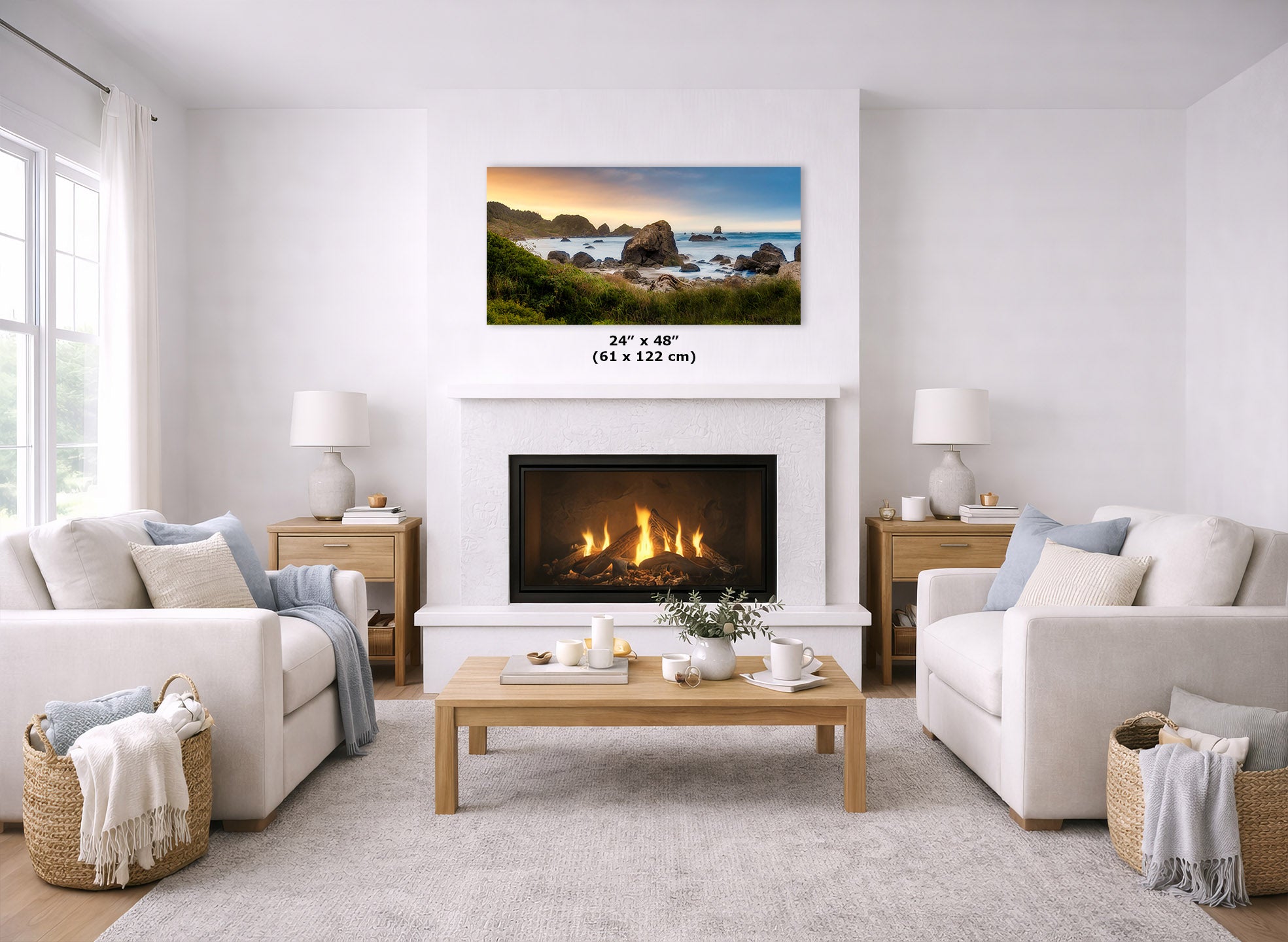 A coastal landscape wall art print is displayed above a fireplace in a bright, modern living room. The print shows a rocky beach and ocean scene with blue water, green cliffs, and a warm sunset sky.