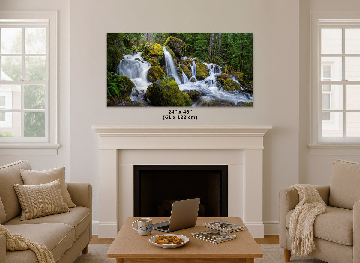 A framed wall art print showing a lush forest waterfall scene, displayed above a white fireplace mantel in a bright, modern living room. The print includes size text indicating 24" x 48" (61 x 122 cm).