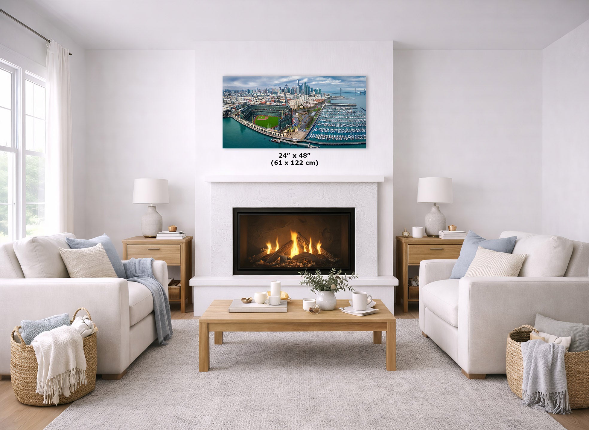 An Oracle Park skyline panorama art print of an aerial photograph of the San Francisco Bay and skyline is displayed on a white wall above a fireplace in a bright, modern living room. The print is shown with a size overlay indicating 24" x 48" (61 x 122 cm).