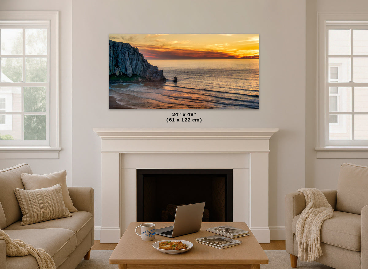 A wall art print showing a coastal sunset over cliffs and beach is displayed above a white fireplace in a bright living room. The print includes size text reading 24 x 48 inches (61 x 122 cm).
