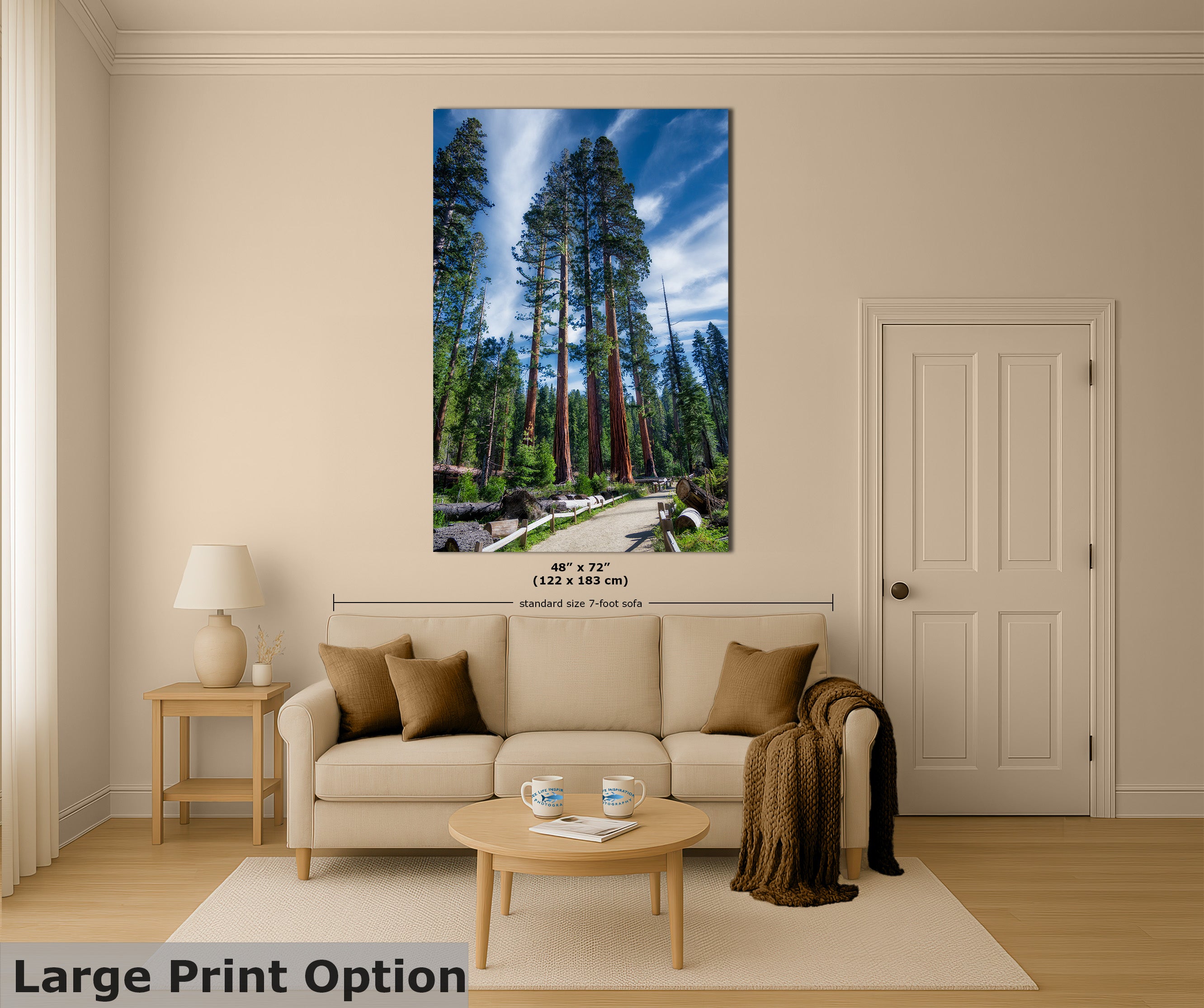 A large vertical wall art print showing a Giant Sequoia forest scene with tall trees and a winding path under a blue sky, displayed above a beige sofa in a styled living room. Small text near the print indicates dimensions, and a bottom-left banner reads 'Large Print Option'.