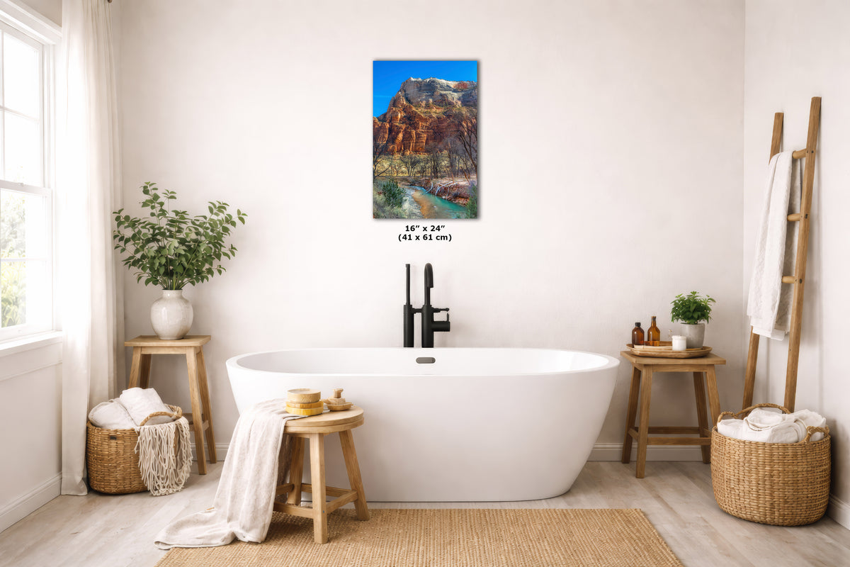 A wall art print depicting a desert canyon landscape with red rock cliffs and blue sky, displayed above a white freestanding bathtub in a bright, neutral bathroom. The print includes size text reading 16 x 24 in (41 x 61 cm).