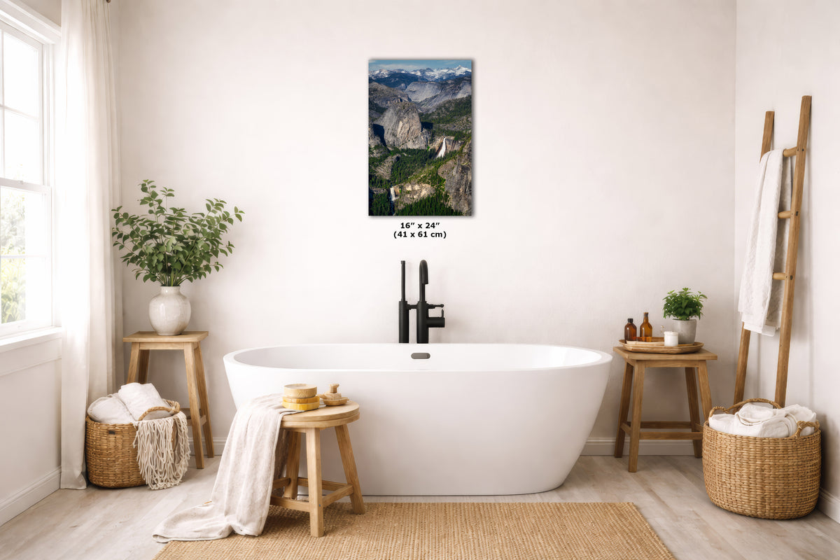 A vertical landscape art print depicting a canyon river scene, displayed on a light beige wall above a white freestanding bathtub in a bright, modern bathroom setting.