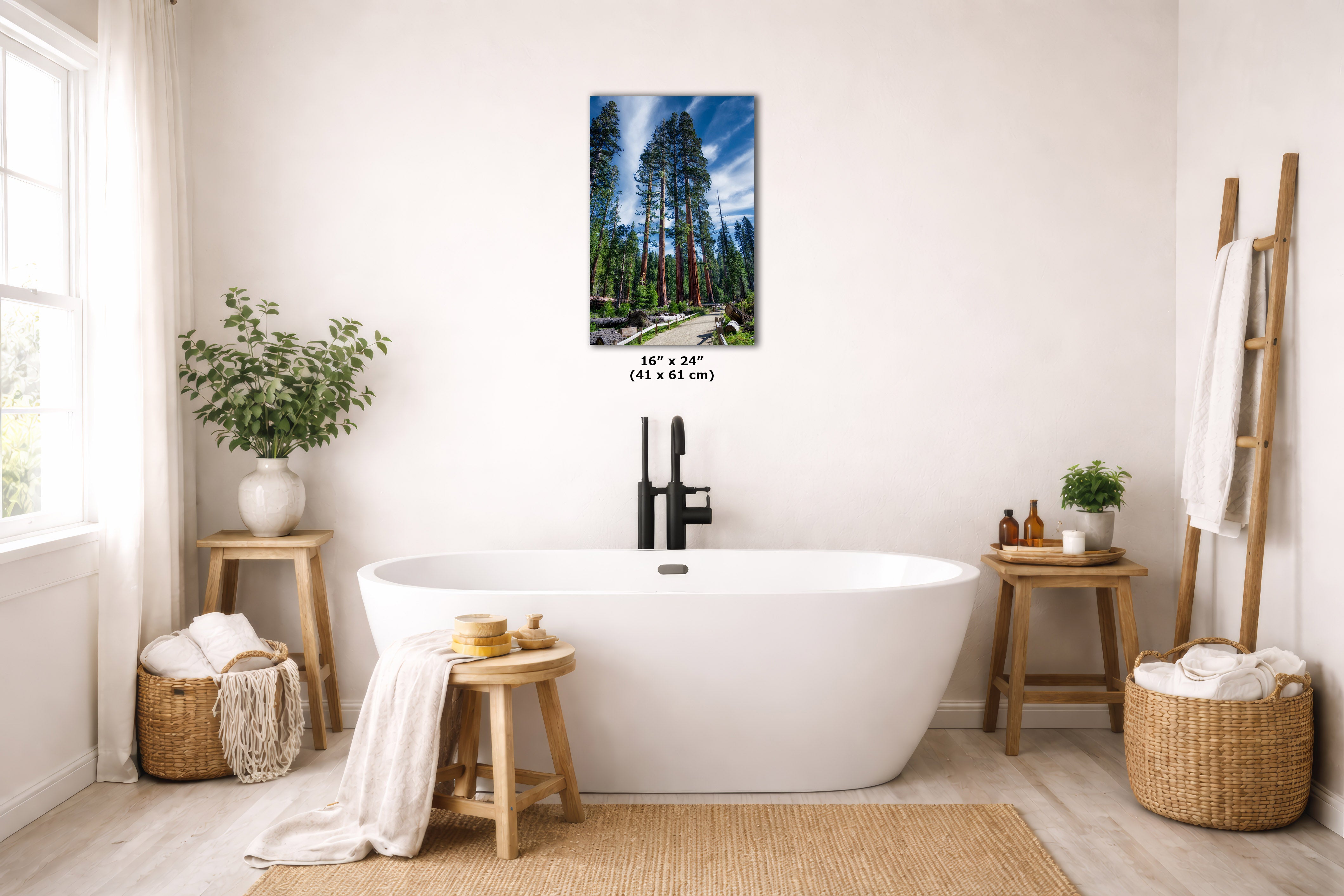 A freestanding white bathtub in a bright, neutral-toned bathroom with a wall-mounted vertical art print showing a forest scene. The print includes size text reading 16 x 24 inches (41 x 61 cm).