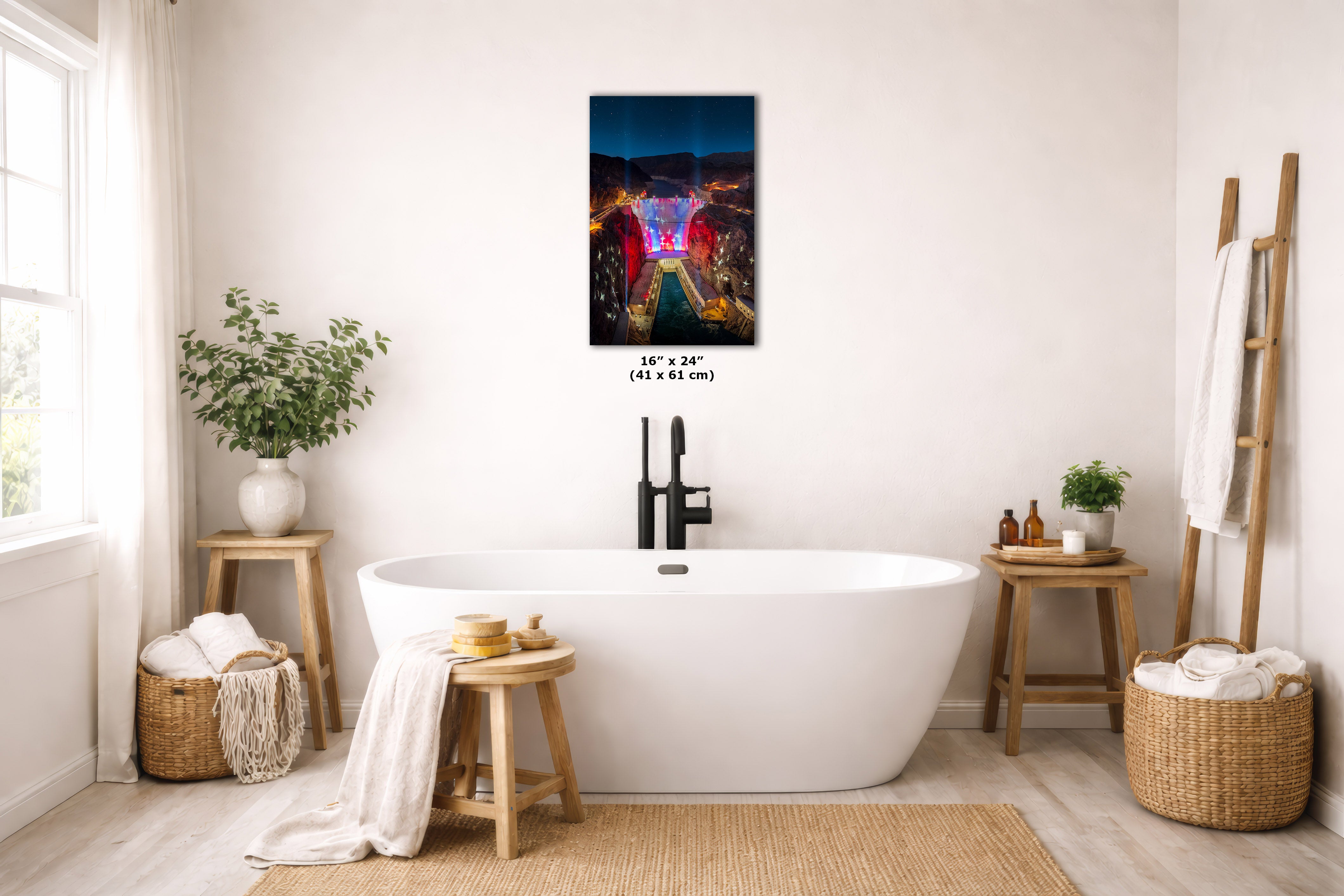 A colorful rectangular wall art print depicting a vibrant night street scene hangs above a white freestanding bathtub in a bright, modern bathroom. The print includes size text reading 16 x 24 in (41 x 61 cm) below it.