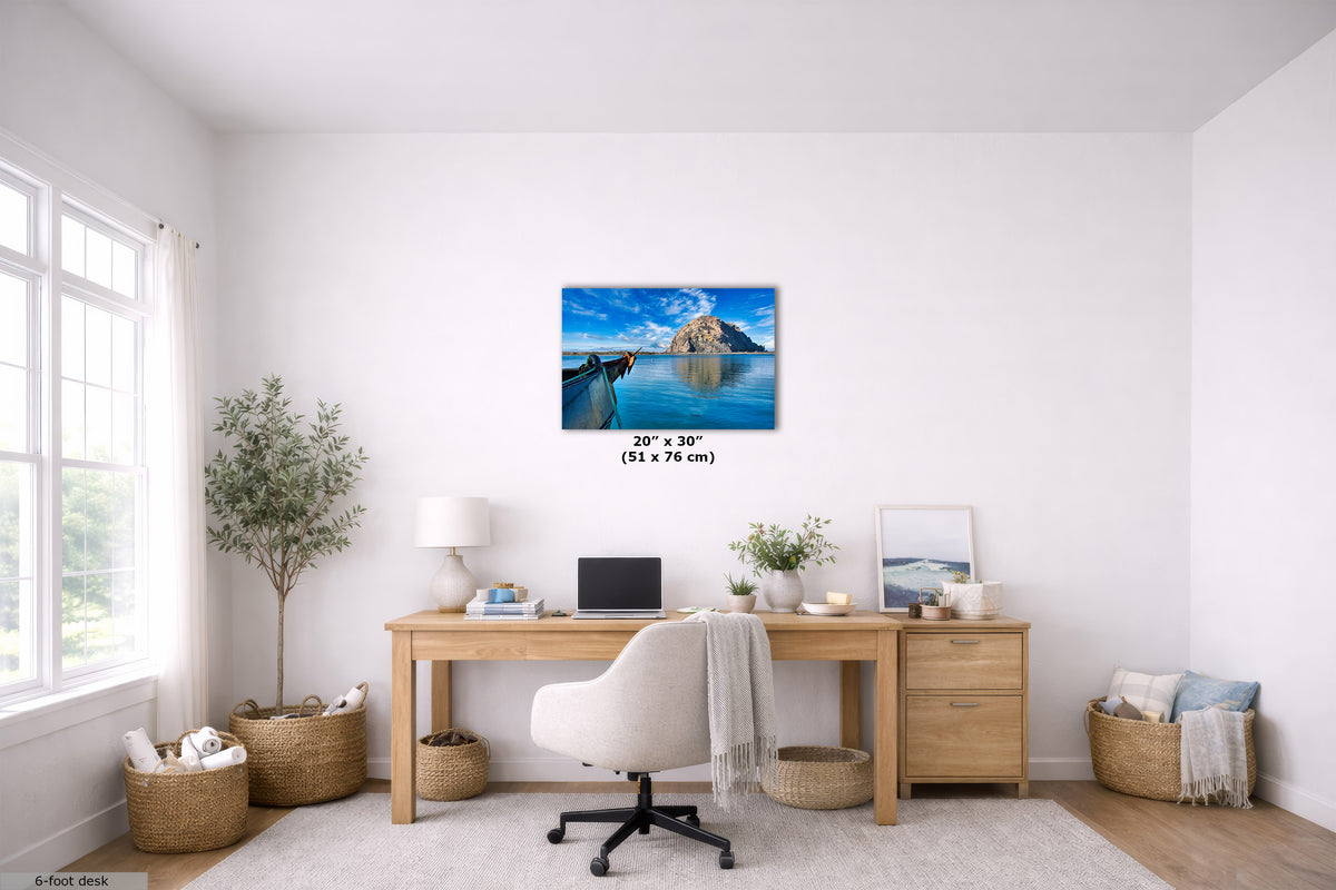 A 20" x 30" canvas print of a scenic coastal island under a blue sky, displayed on a white wall in a bright, modern home office setting above a wooden desk.