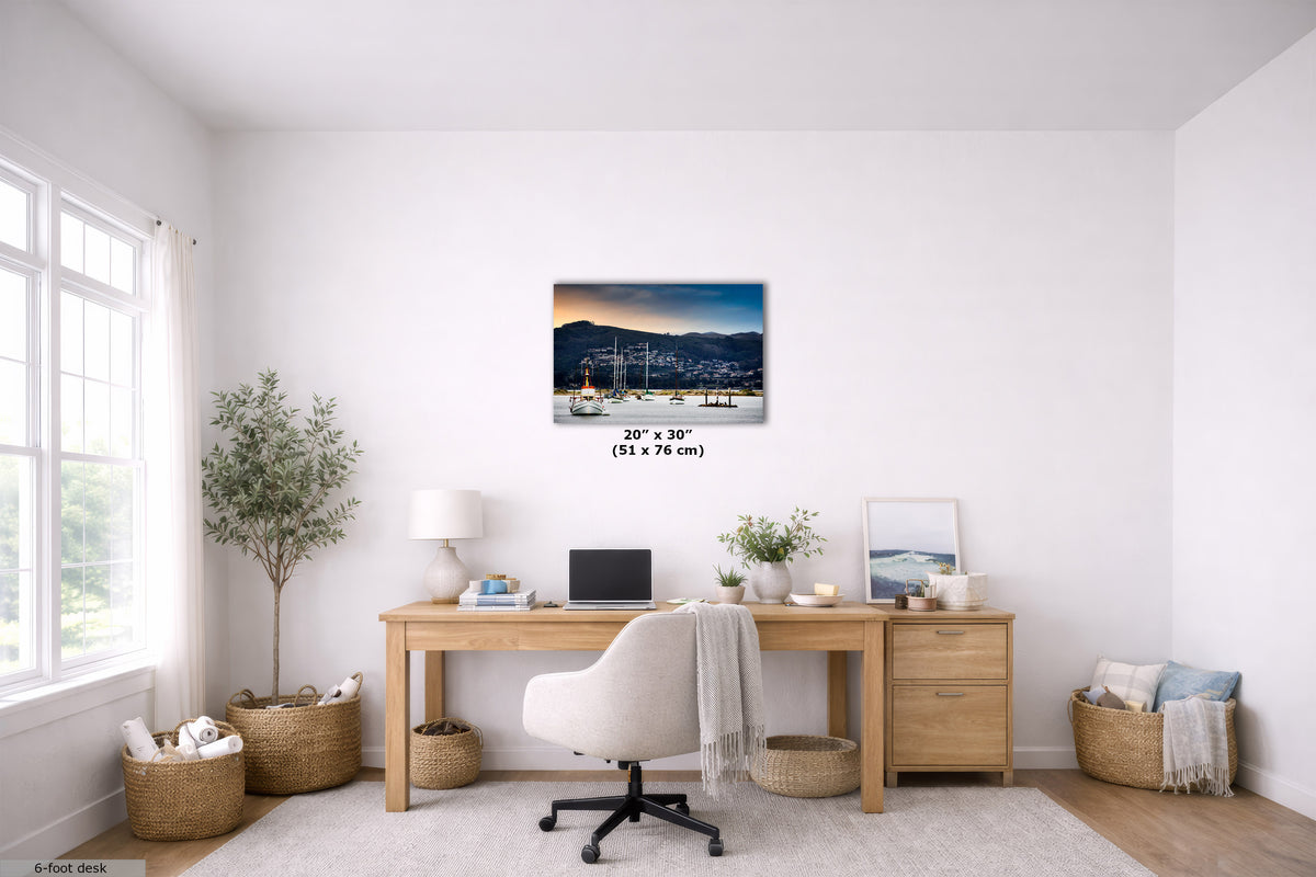 A framed wall art print depicting a harbor city at dusk is displayed above a wooden desk in a bright, modern home office. The print is shown with a size overlay indicating 20" x 30" (51 x 76 cm).