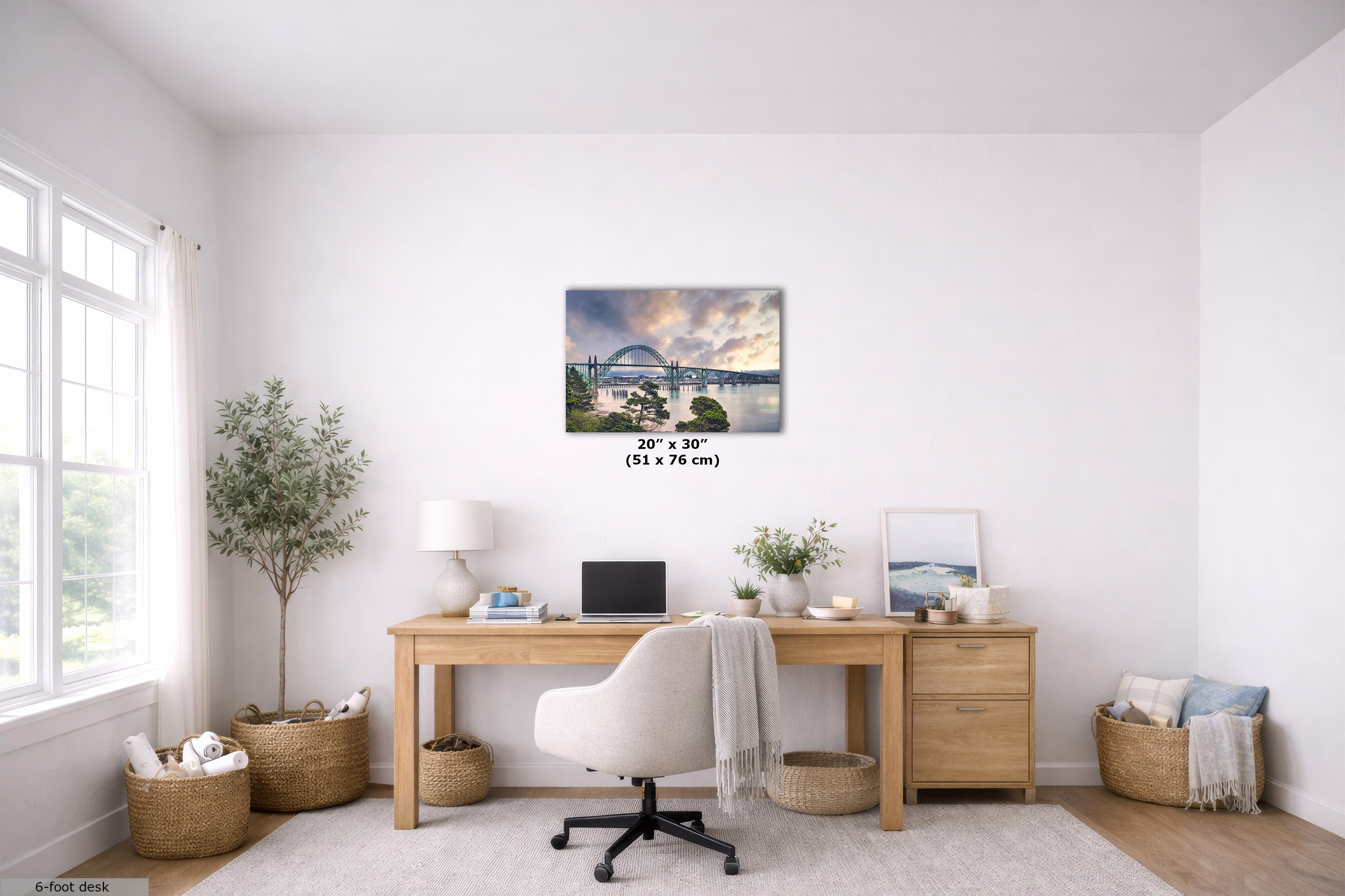 A wall art print depicting a scenic bridge over water under a dramatic sunset sky, displayed in a bright, modern home office setting above a wooden desk with a white office chair.