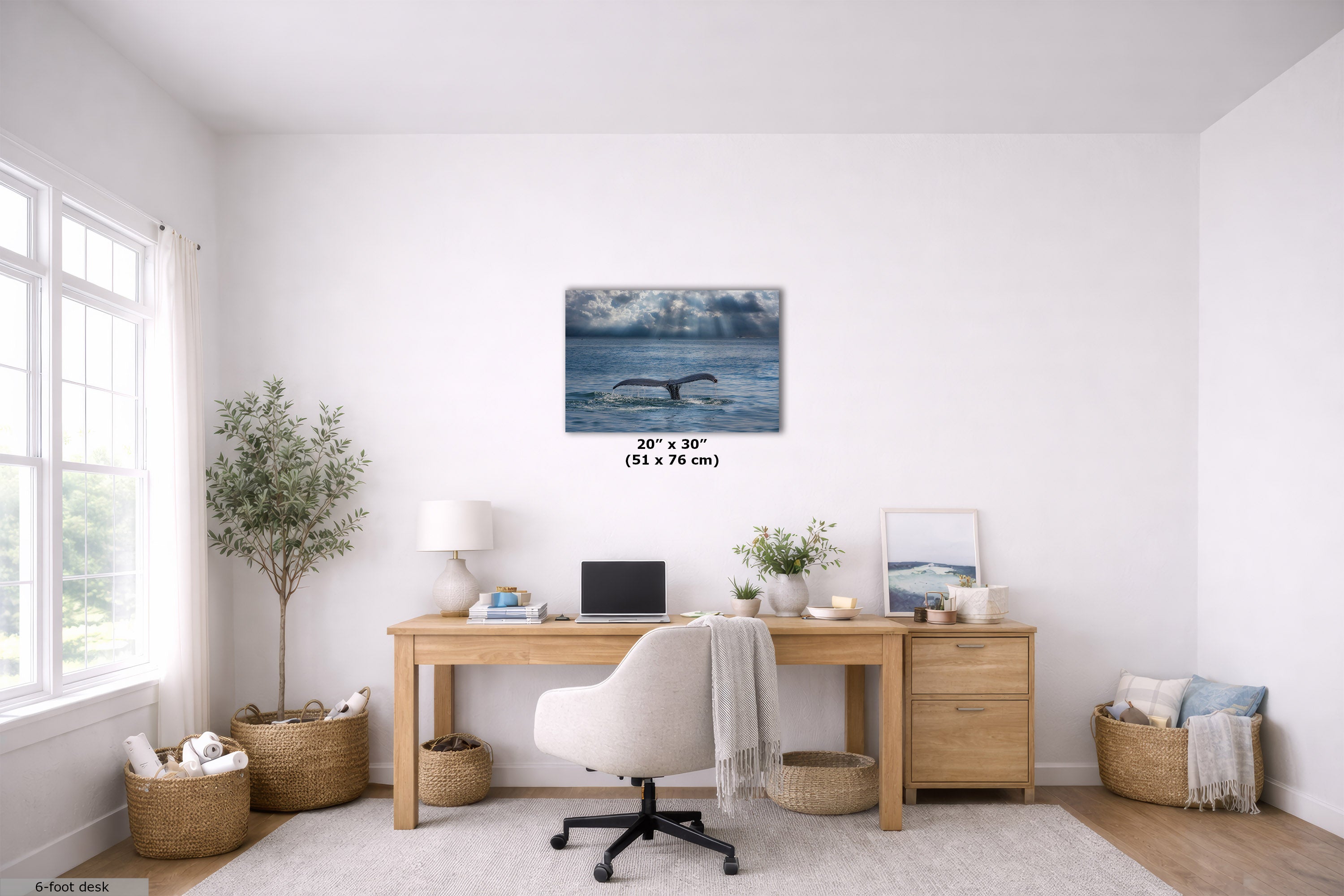 A wall art print depicting a whale in blue ocean waters under a cloudy sky, displayed in a bright, modern home office setting above a wooden desk.